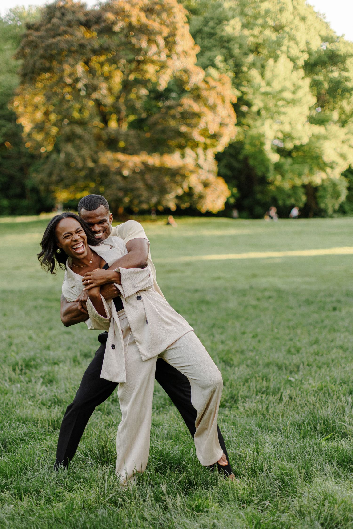 A playful couple embracing and laughing together in a sunny park.