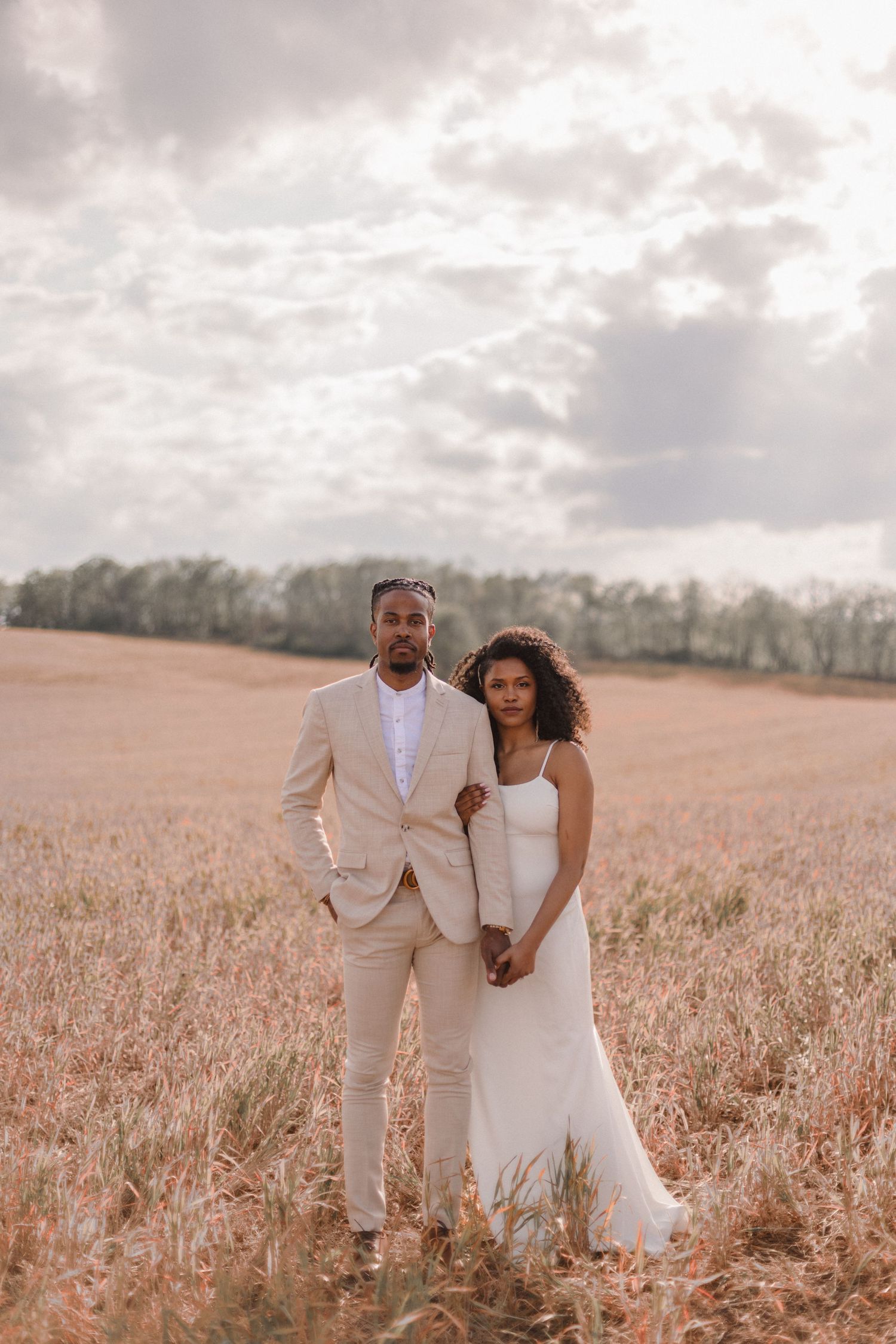 A couple poses for a formal portrait in a golden wheat field at sunset.