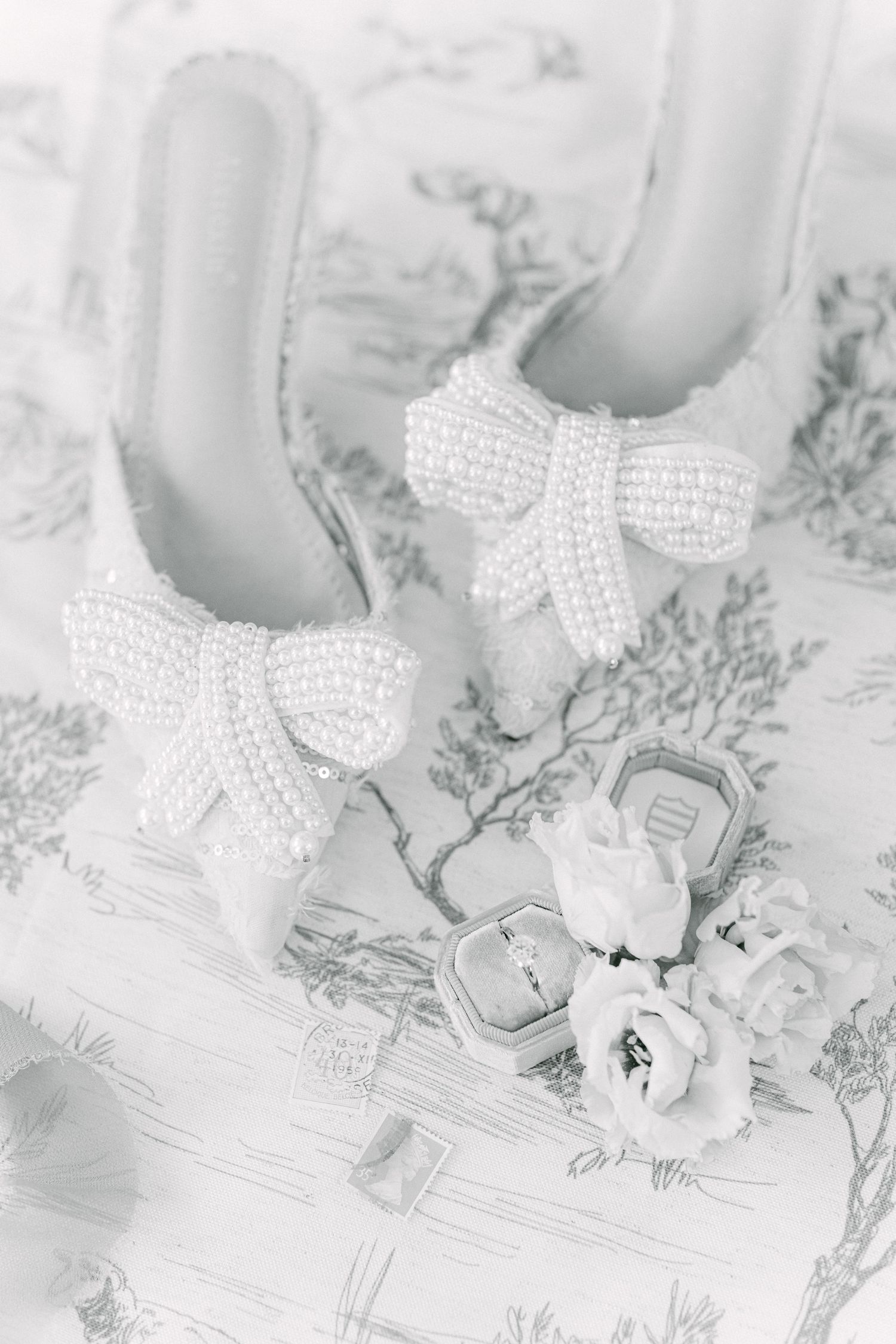 Elegant white beaded bridal shoes with floral details on patterned background.