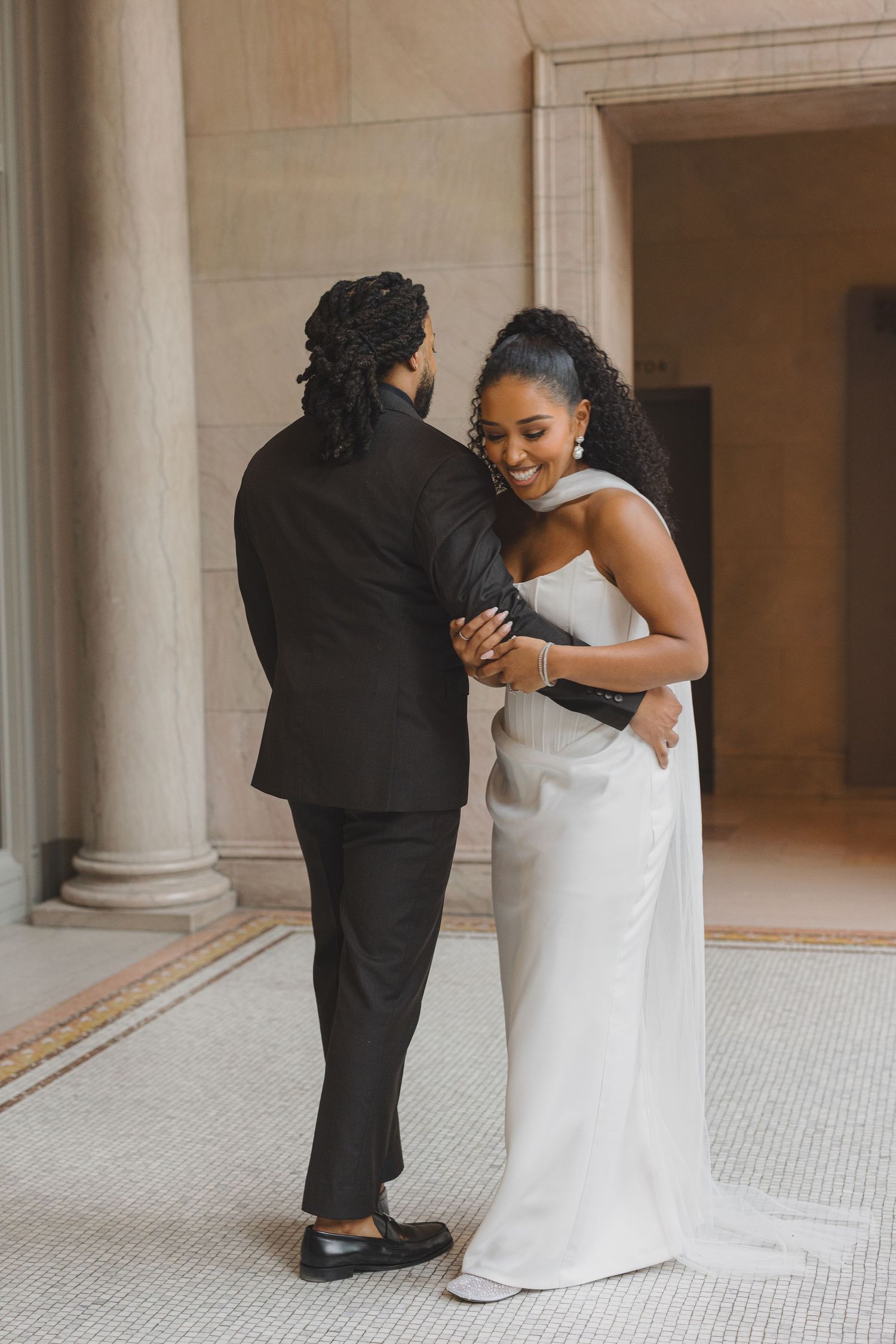 A sequence of four wedding photos showing a couple in black and white attire embracing in an elegant columned hall.