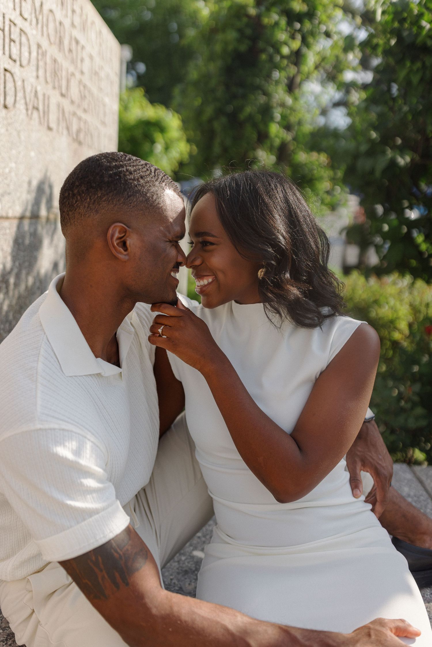 Intimate couple in white outfits share a tender moment while sitting outdoors.
