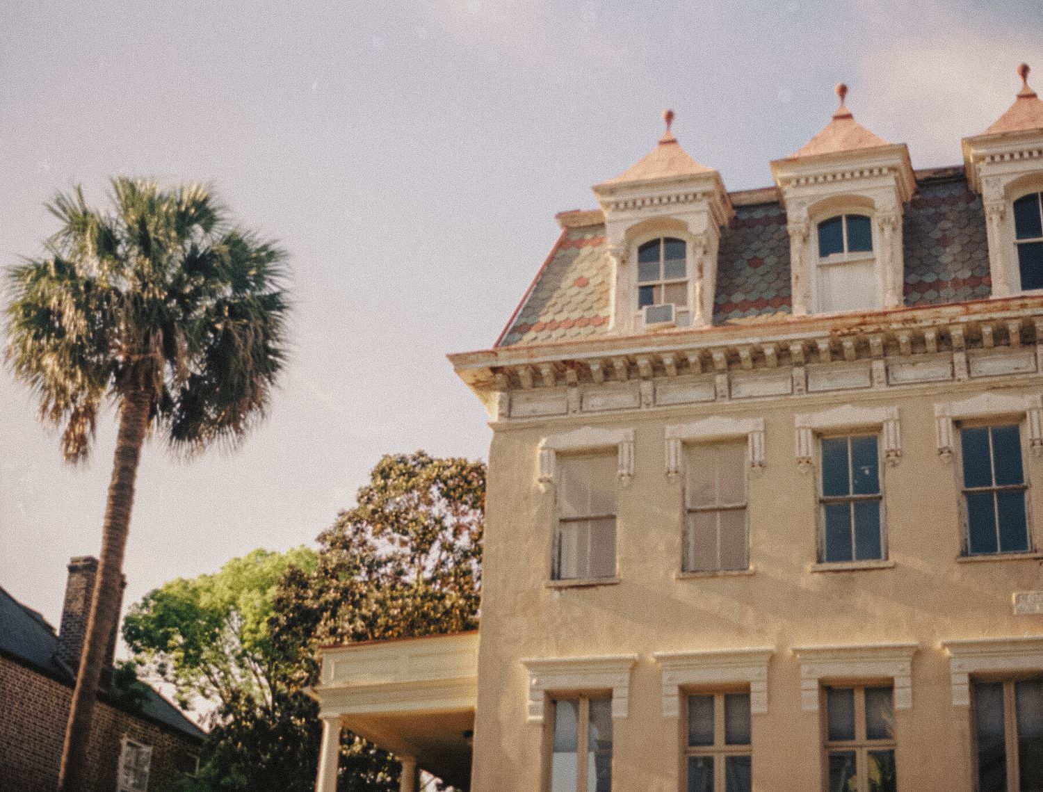 Historic Charleston mansion with ornate Second Empire architecture and a palm tree against a soft sunset sky.