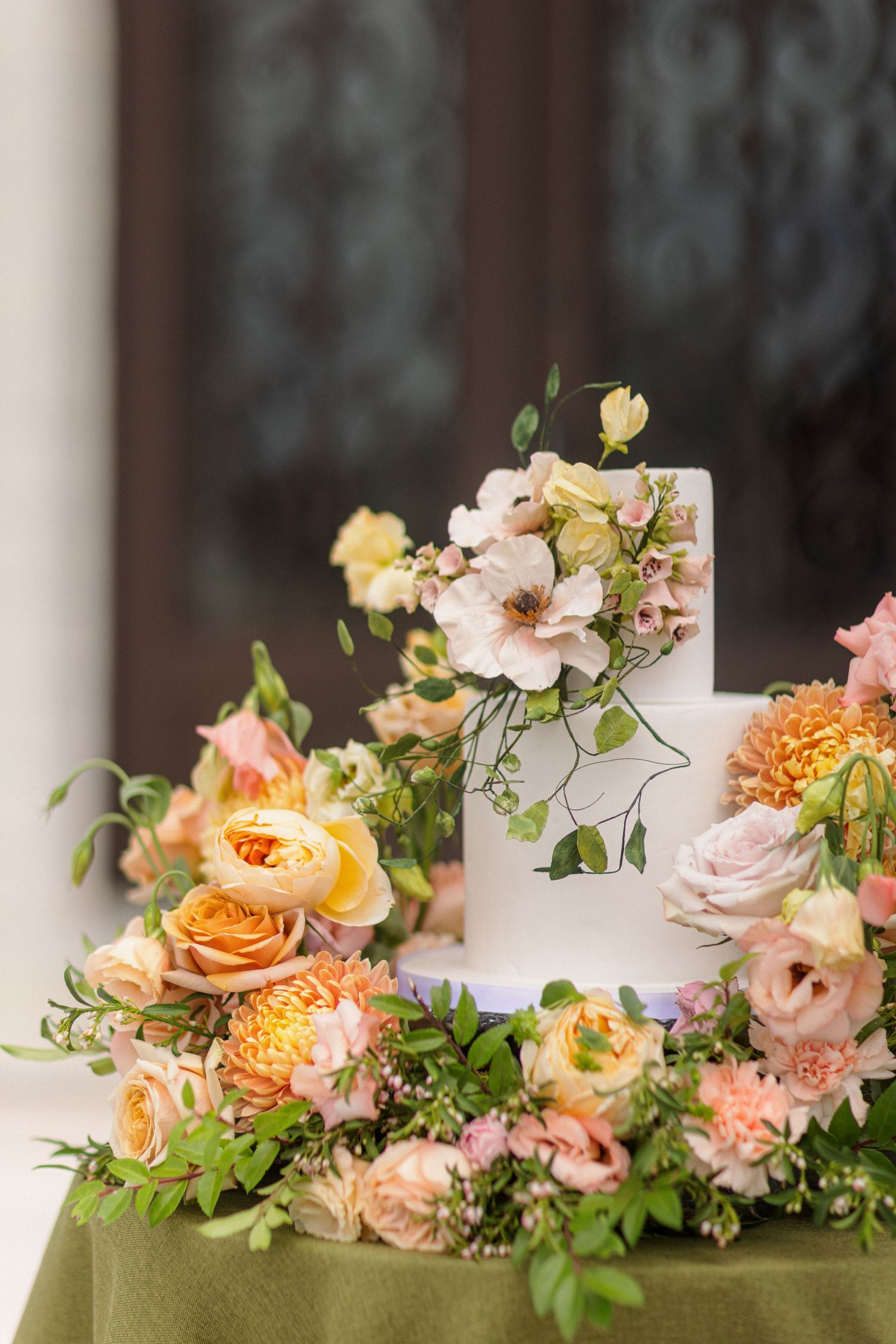 White wedding cake decorated with cascading peach and pink flowers against a dark background.