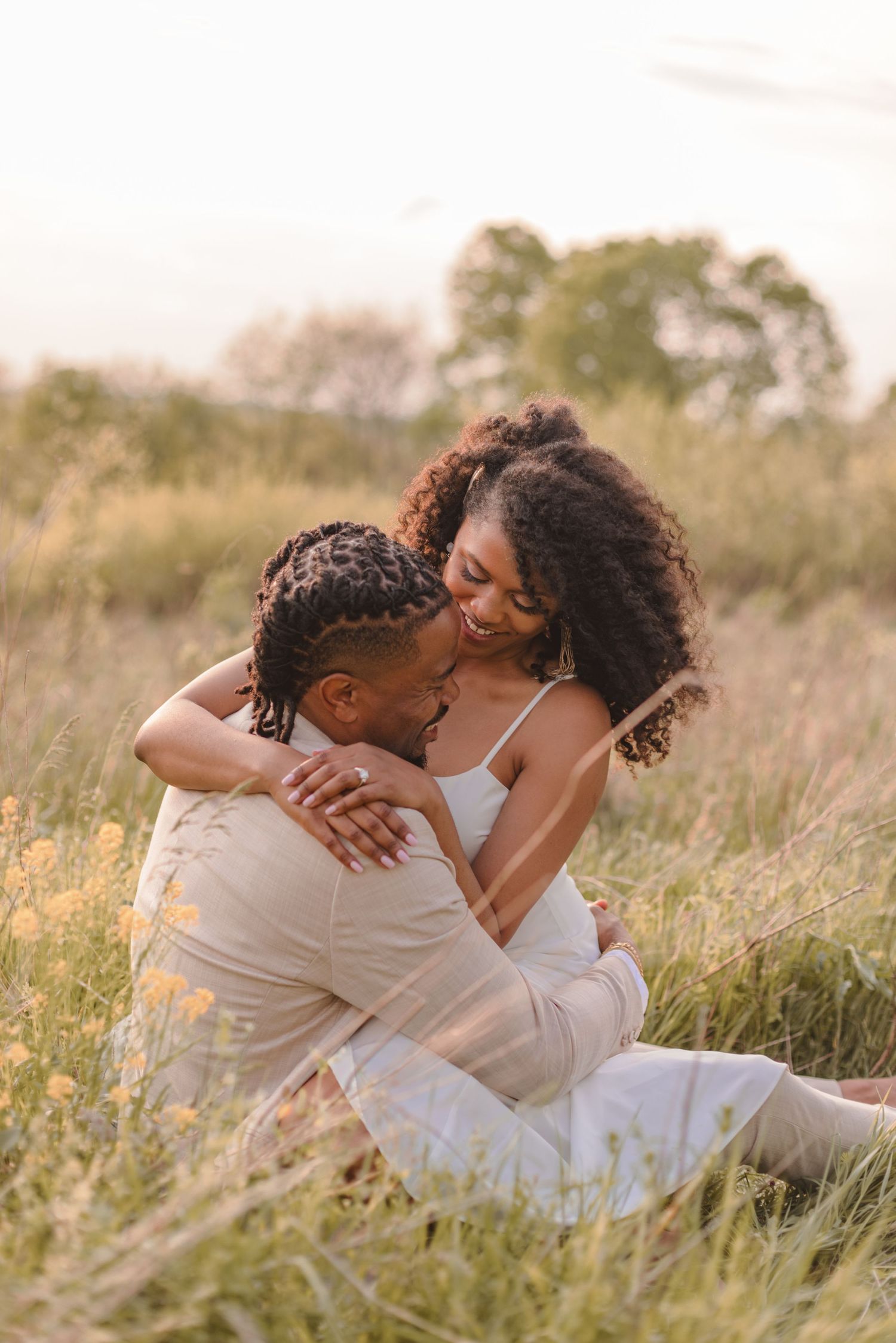 A couple shares an intimate embrace while sitting in tall grass during golden hour.
