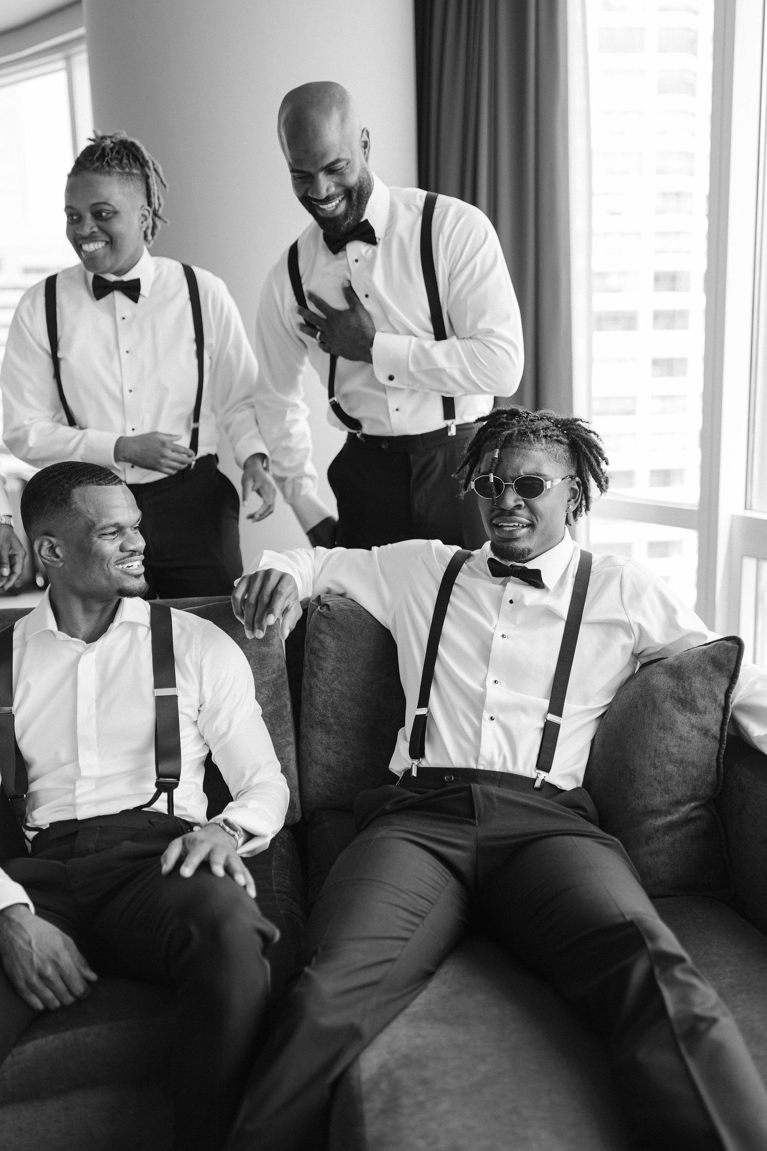 Wedding party in classic black and white attire relaxing on modern grey furniture.