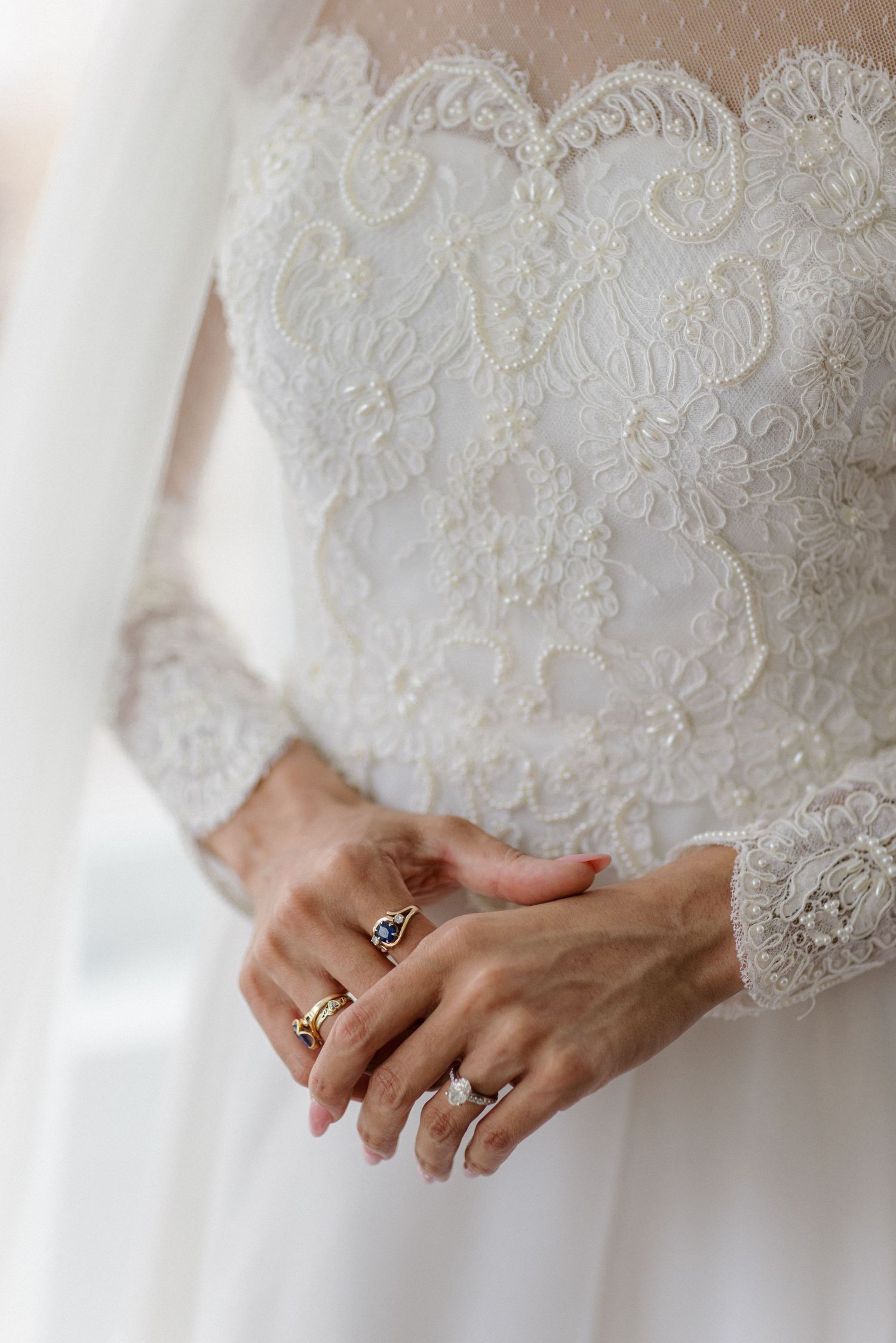 Close-up of hands wearing wedding rings against intricate white lace wedding dress detail.