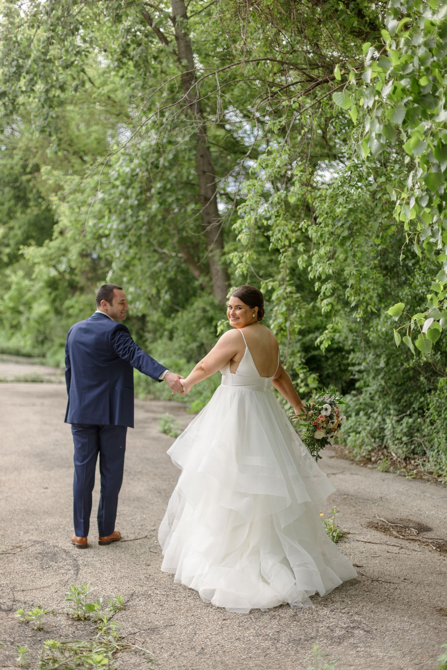 Couple walking hand in hand on nature path with flowing white wedding gown.