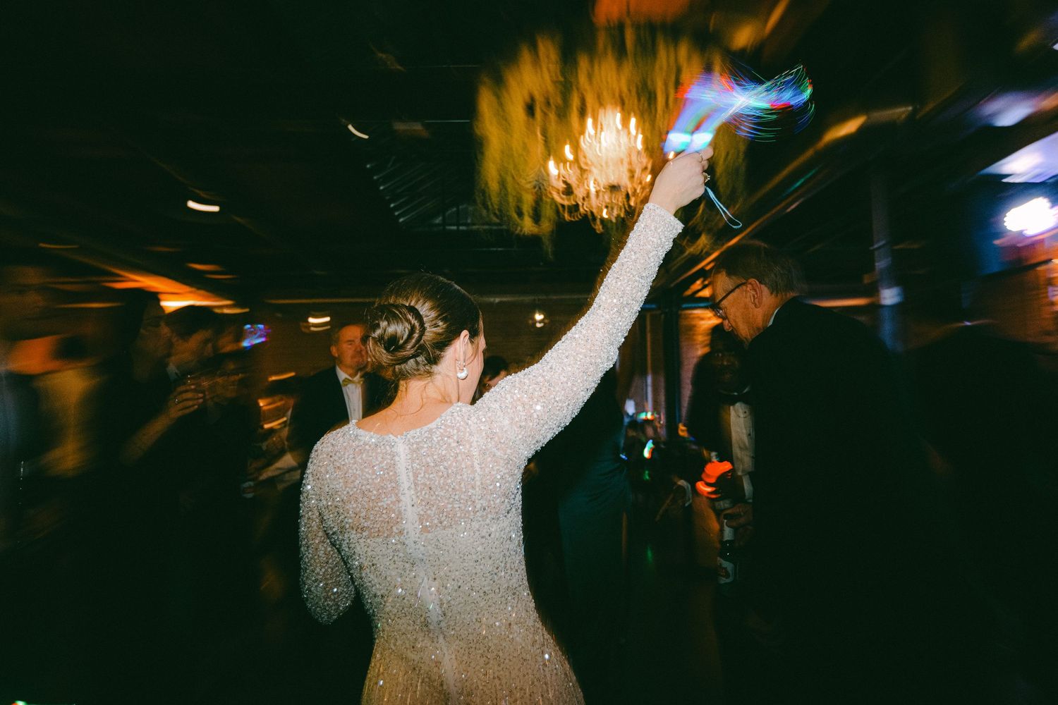 Dancing figure in white dress celebrating at dimly lit wedding reception.