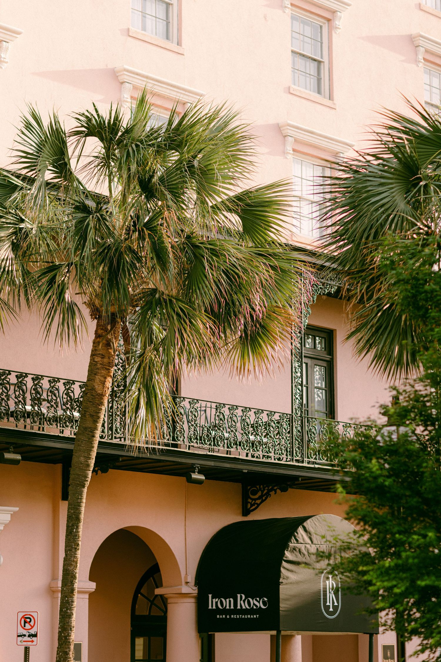 Historic pink building with ornate wrought iron balconies and palm trees along a Charleston street.