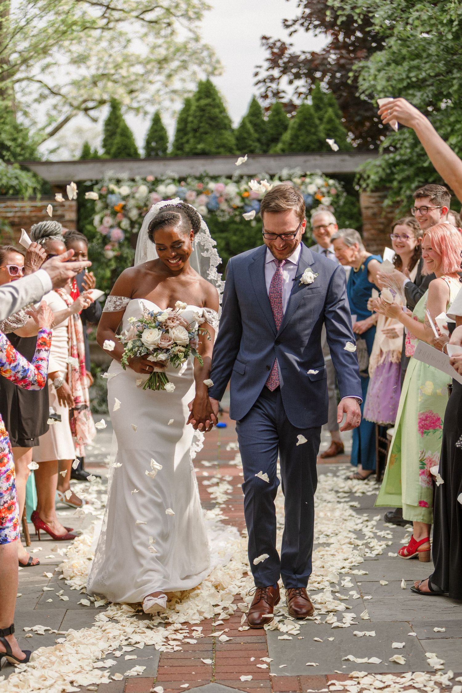 Newlyweds walking down aisle while guests throw flower petals in celebration.