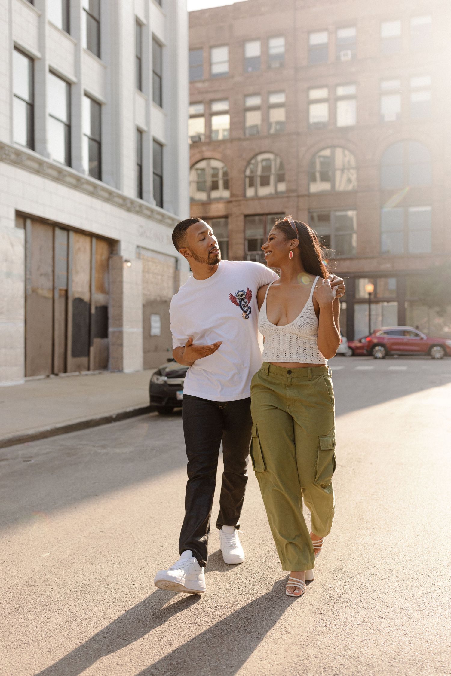 A couple laughs together while walking down a sunny urban street.