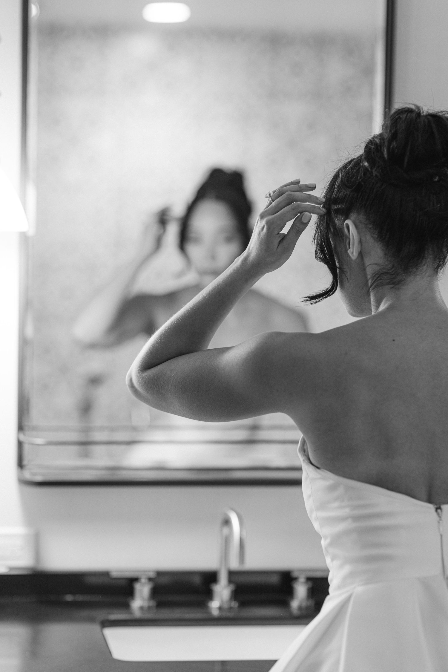 Black and white photo capturing wedding day preparation in mirror reflection.