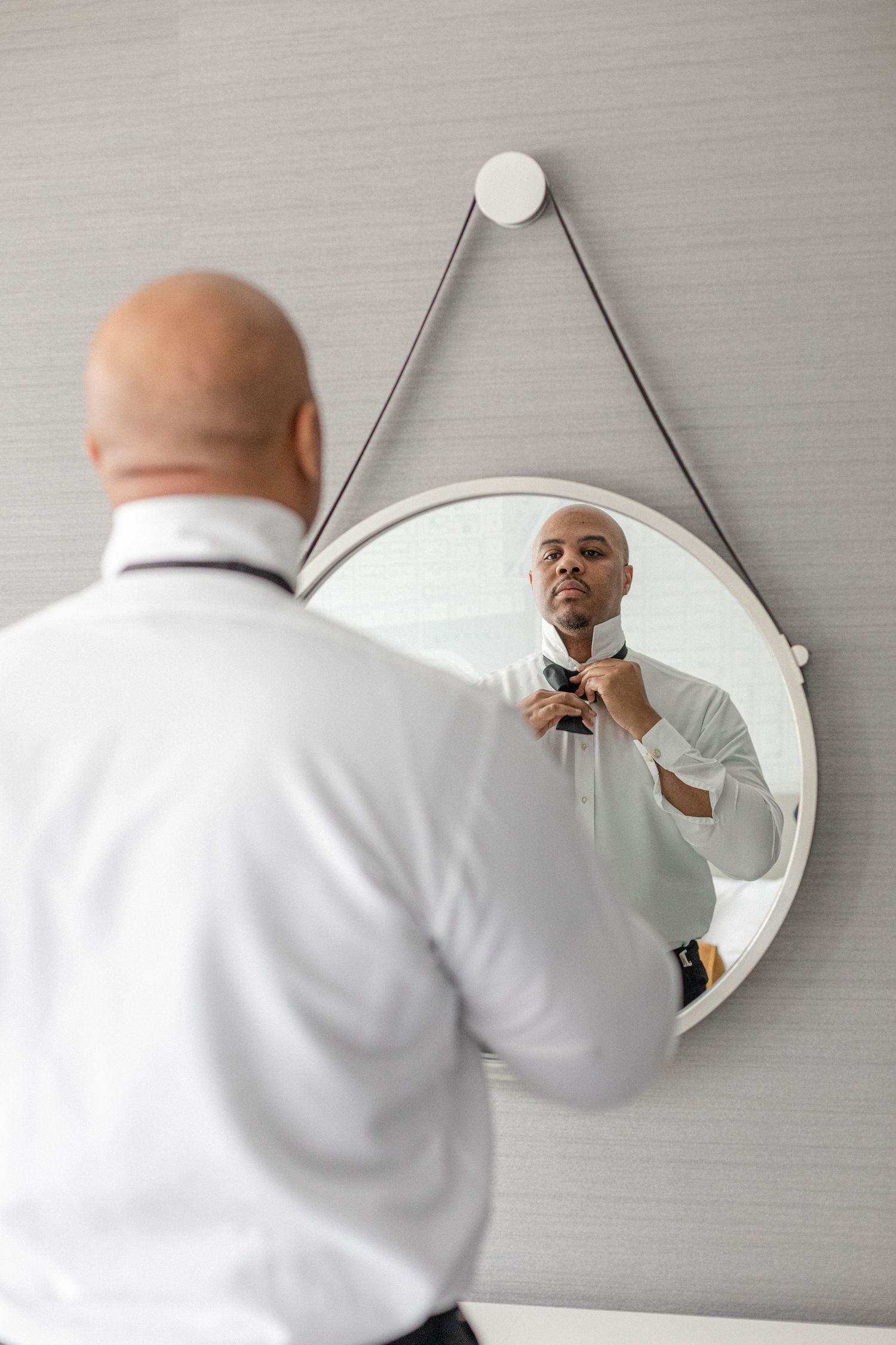 A reflection of someone adjusting their tie in a round hanging mirror.