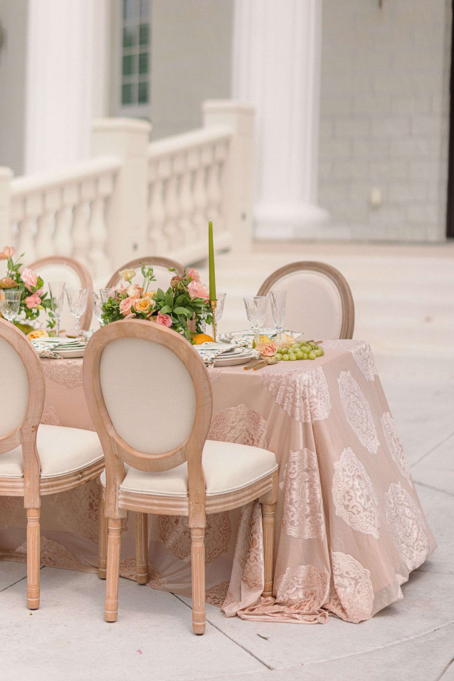 Elegant table settings with blush pink chairs and lace tablecloths in a light-filled venue create a romantic atmosphere.