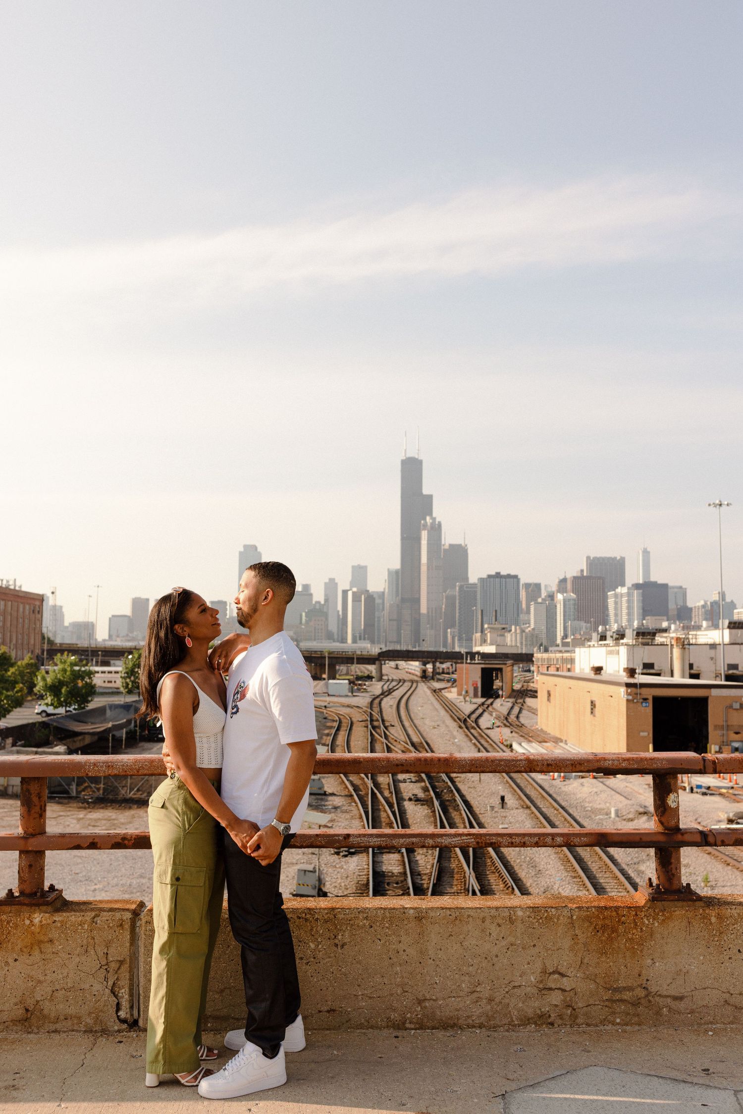 A romantic couple embraces on a rooftop with the Chicago skyline visible in the background during sunset.