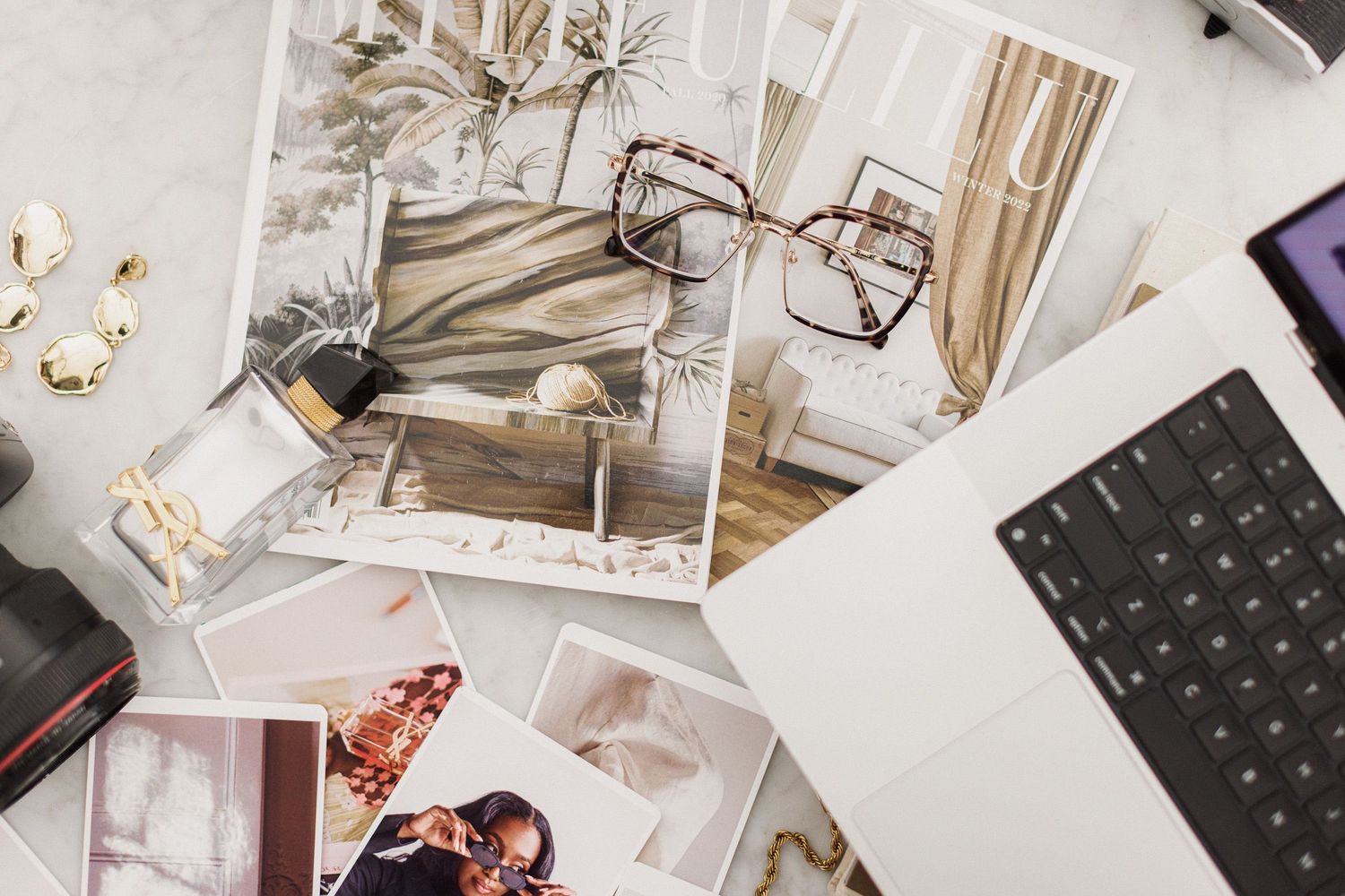 Scattered photographs and a laptop keyboard on a white surface with vintage-style glasses and personal items.