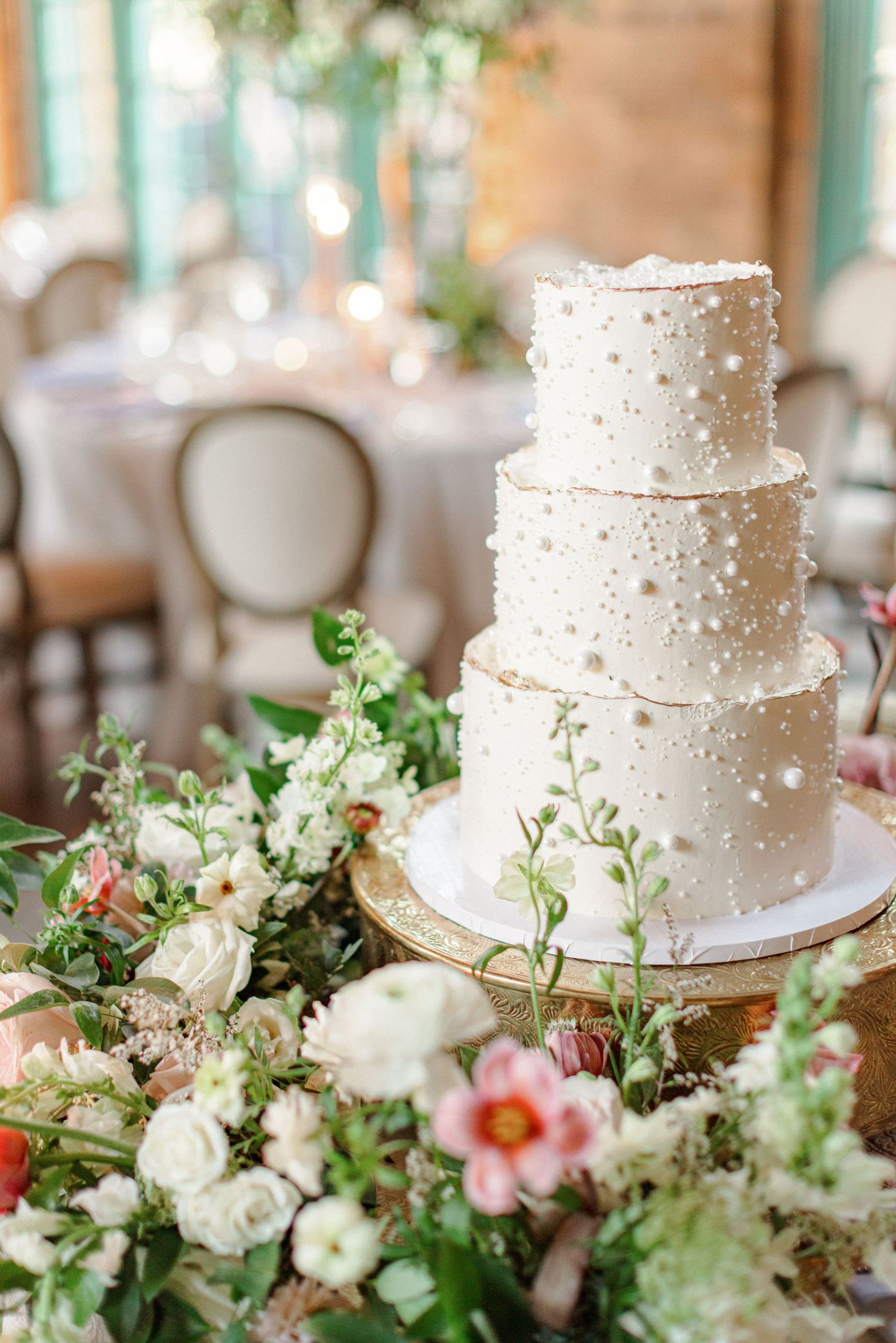Elegant white wedding cake decorated with pearls and fresh flowers on display.