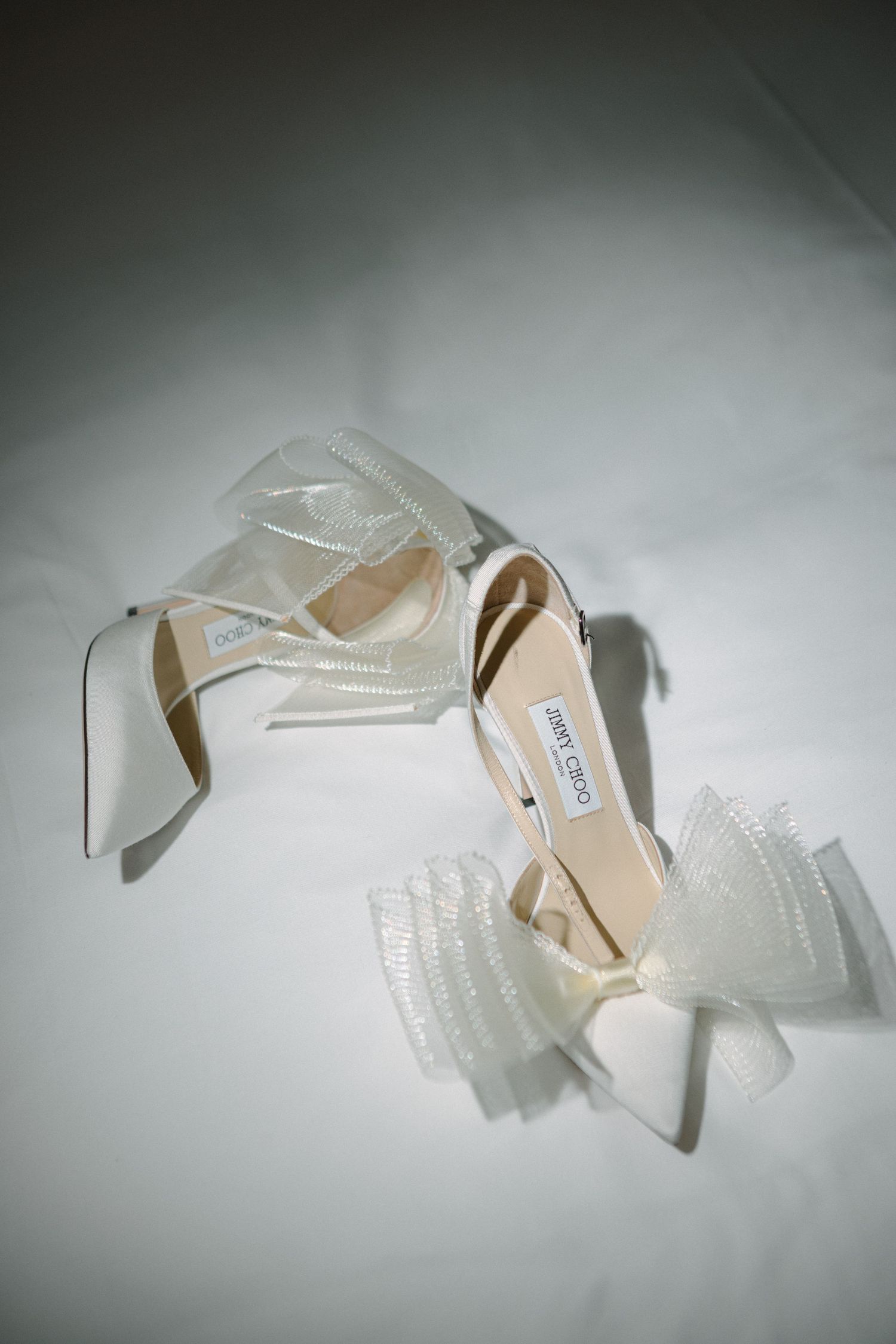 Designer white wedding heels with bow detail captured in dramatic lighting.
