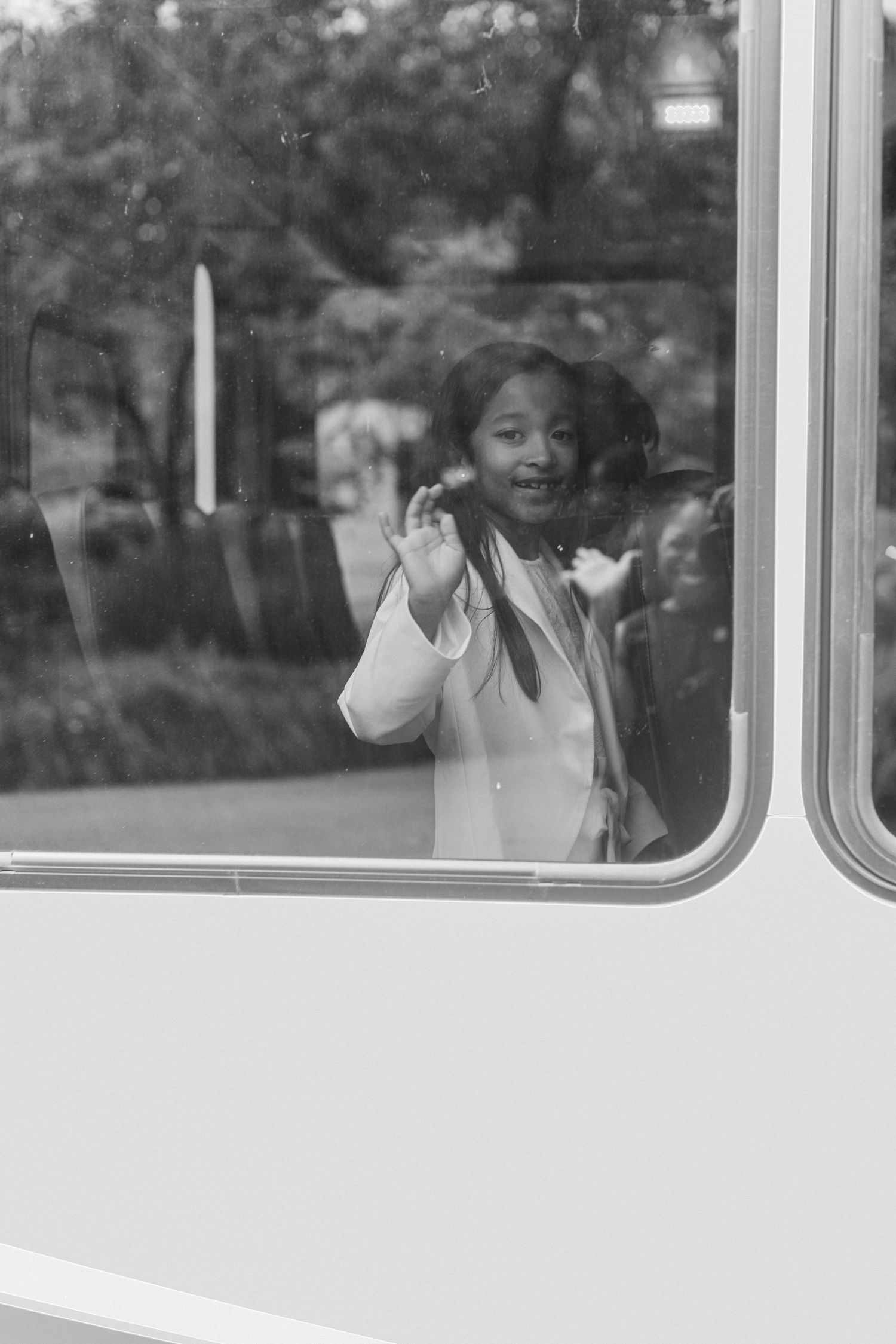 A black and white photo of someone waving through a train window.