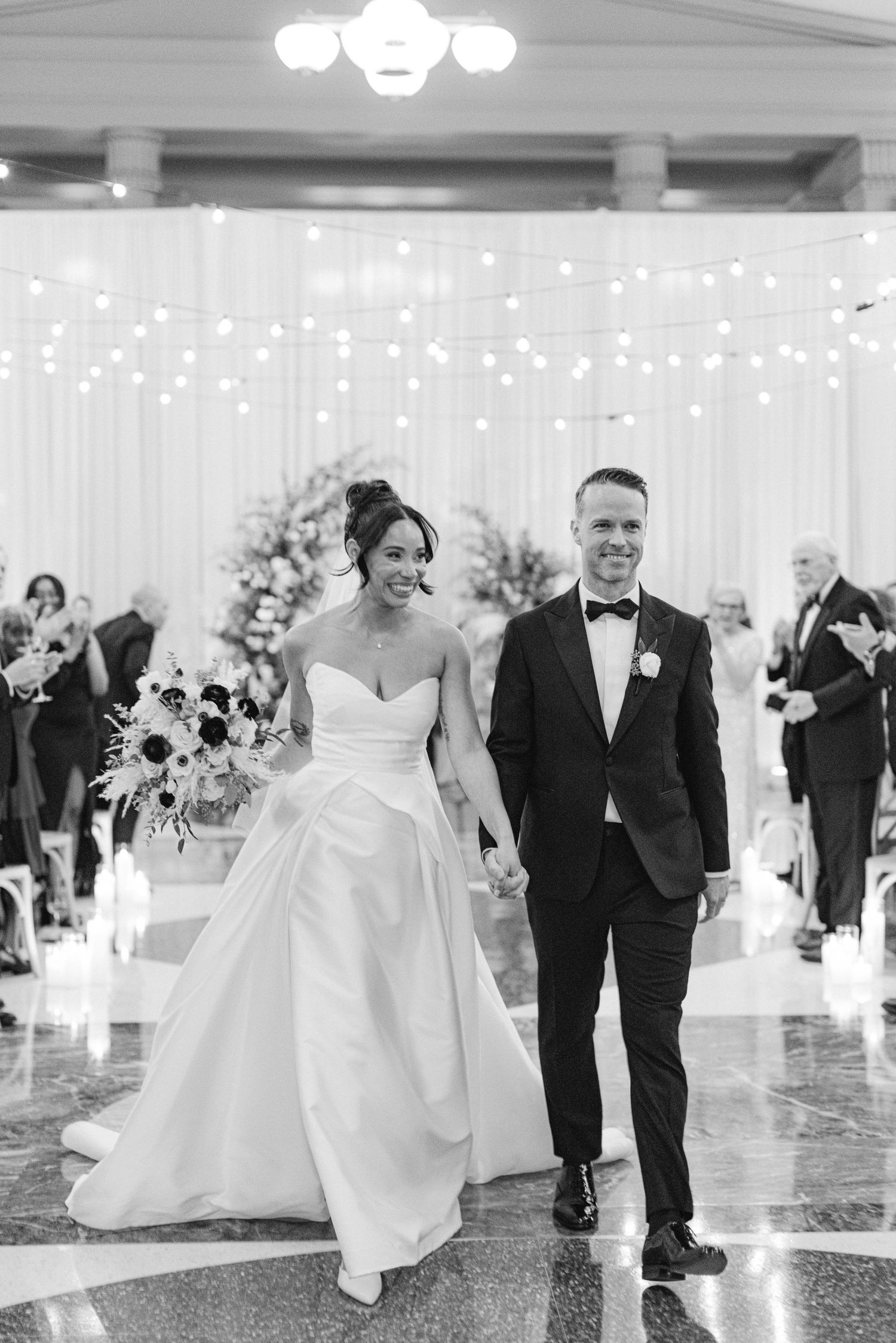 Wedding celebration in an elegant ballroom with string lights and white decor.