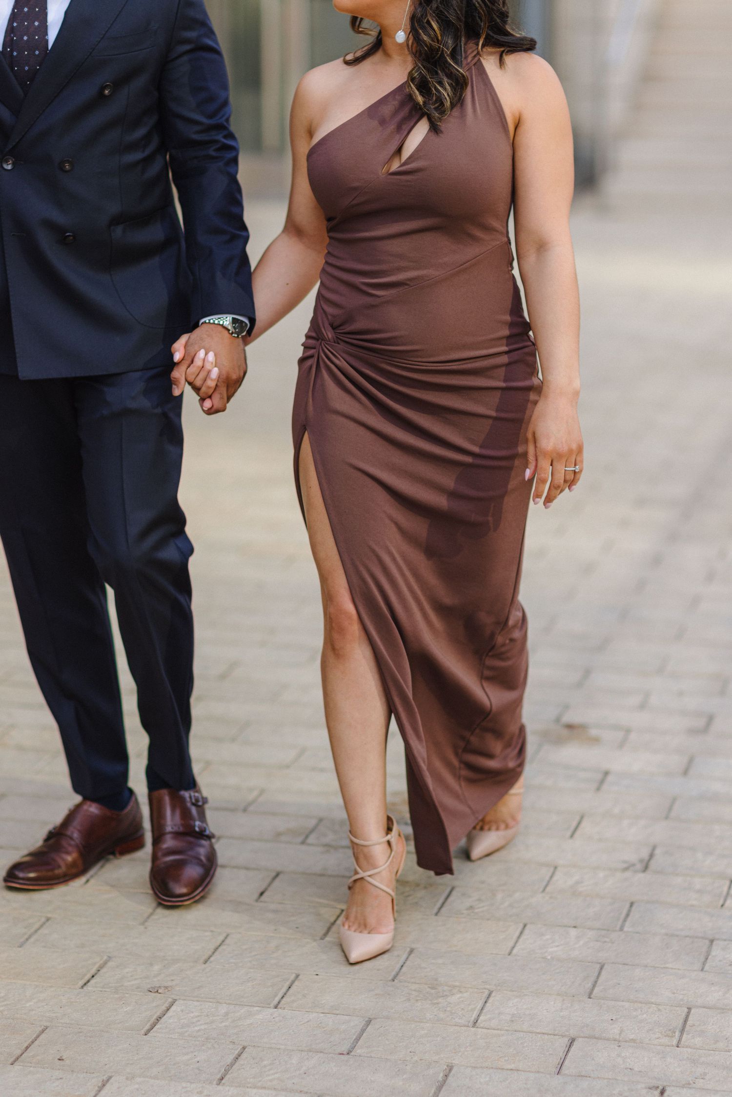 Couple holding hands showing elegant formal attire with brown satin dress and navy suit.