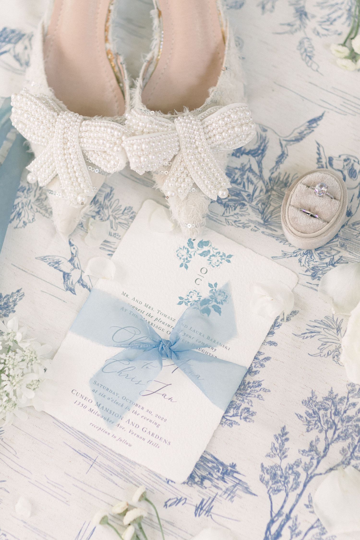 White bow-adorned bridal shoes displayed with blue floral wedding invitations.