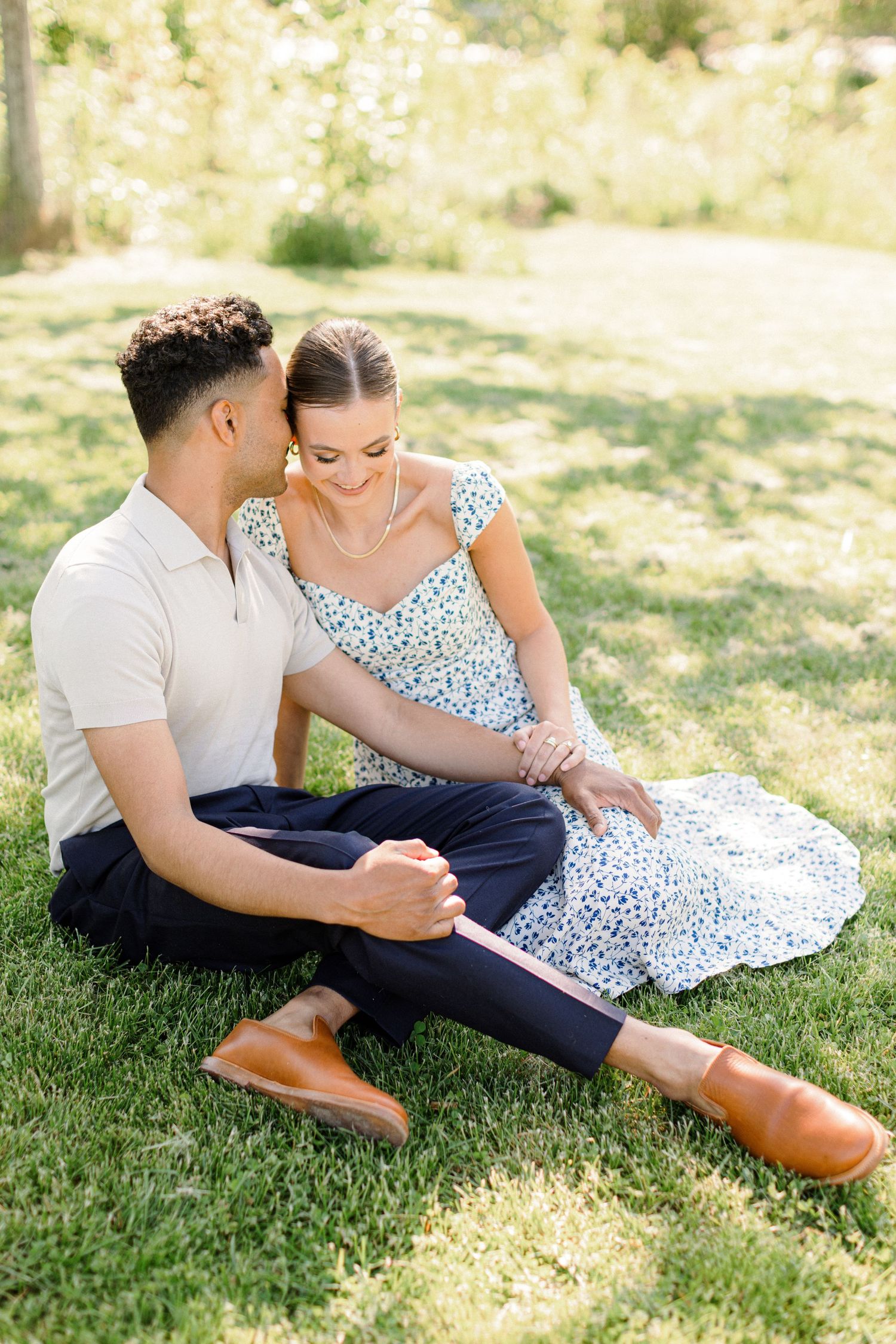 A couple relaxing on grass, wearing coordinated casual outfits with blue floral dress.