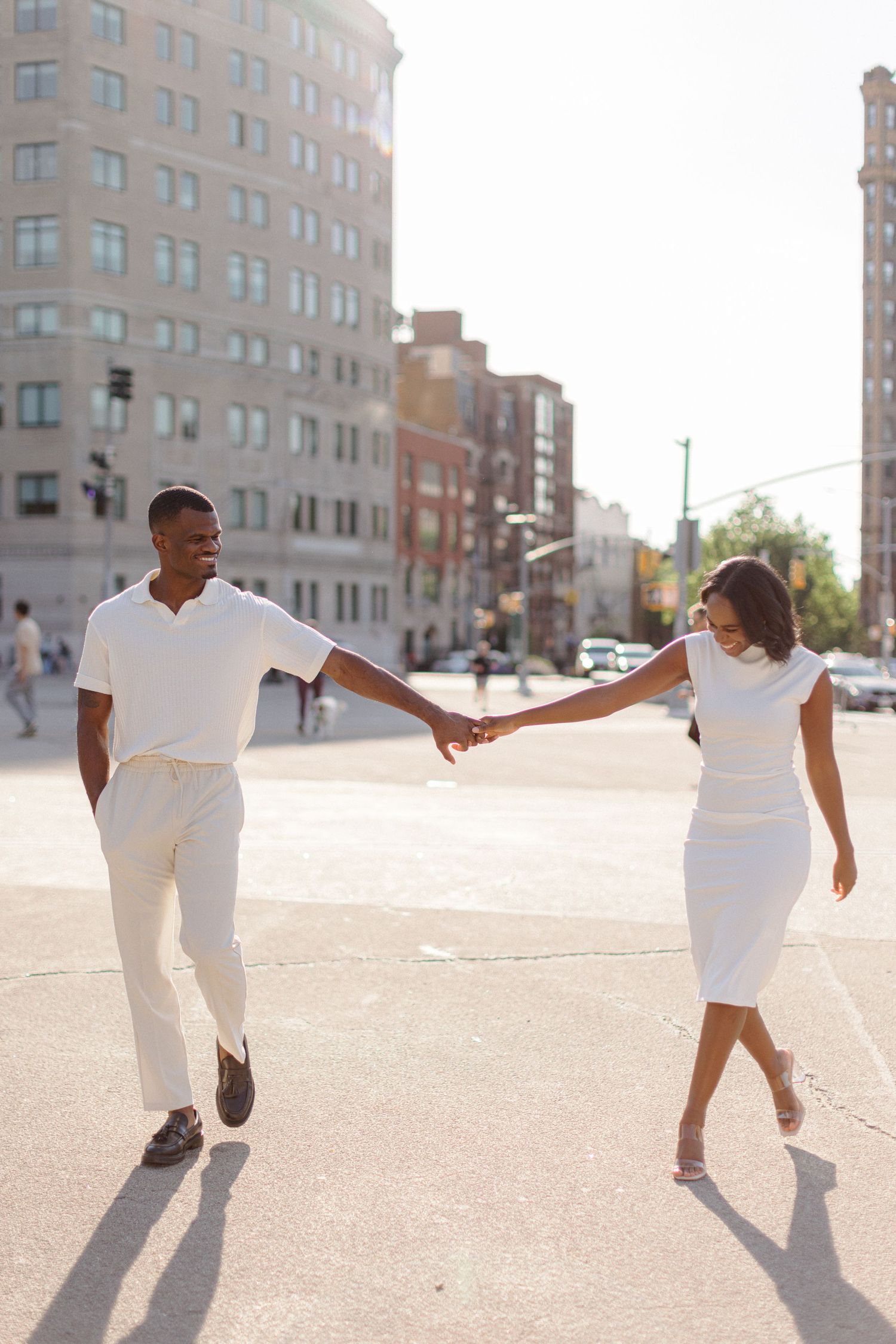 A couple in coordinated white outfits dancing together on a city street.