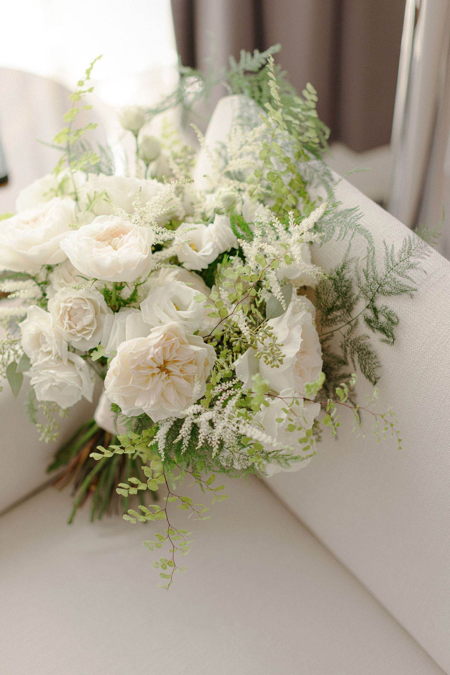 Elegant white wedding bouquet with roses and delicate greenery against a light background.