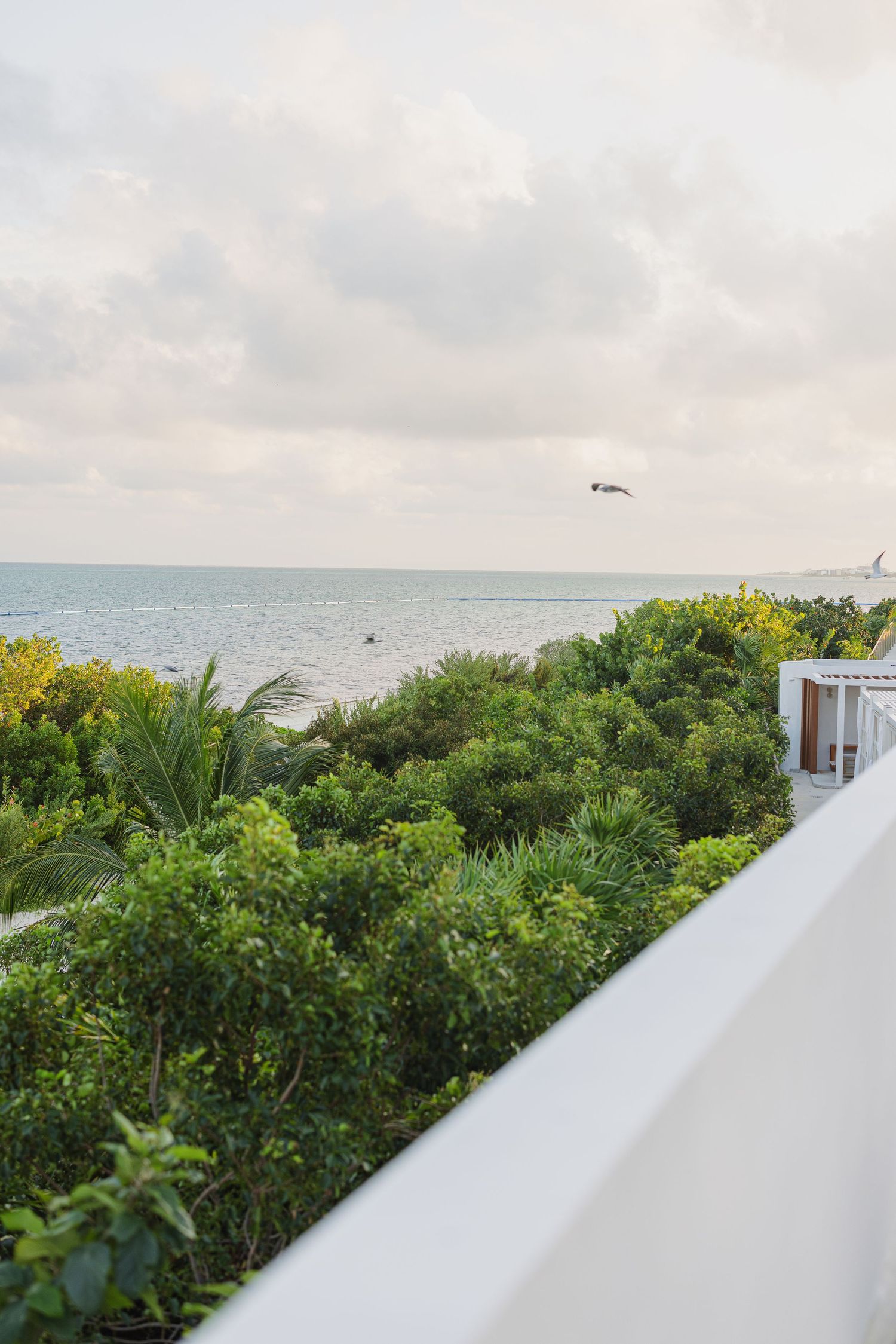 Panoramic view of a coastal landscape with lush greenery and white architectural elements against a cloudy sky.
