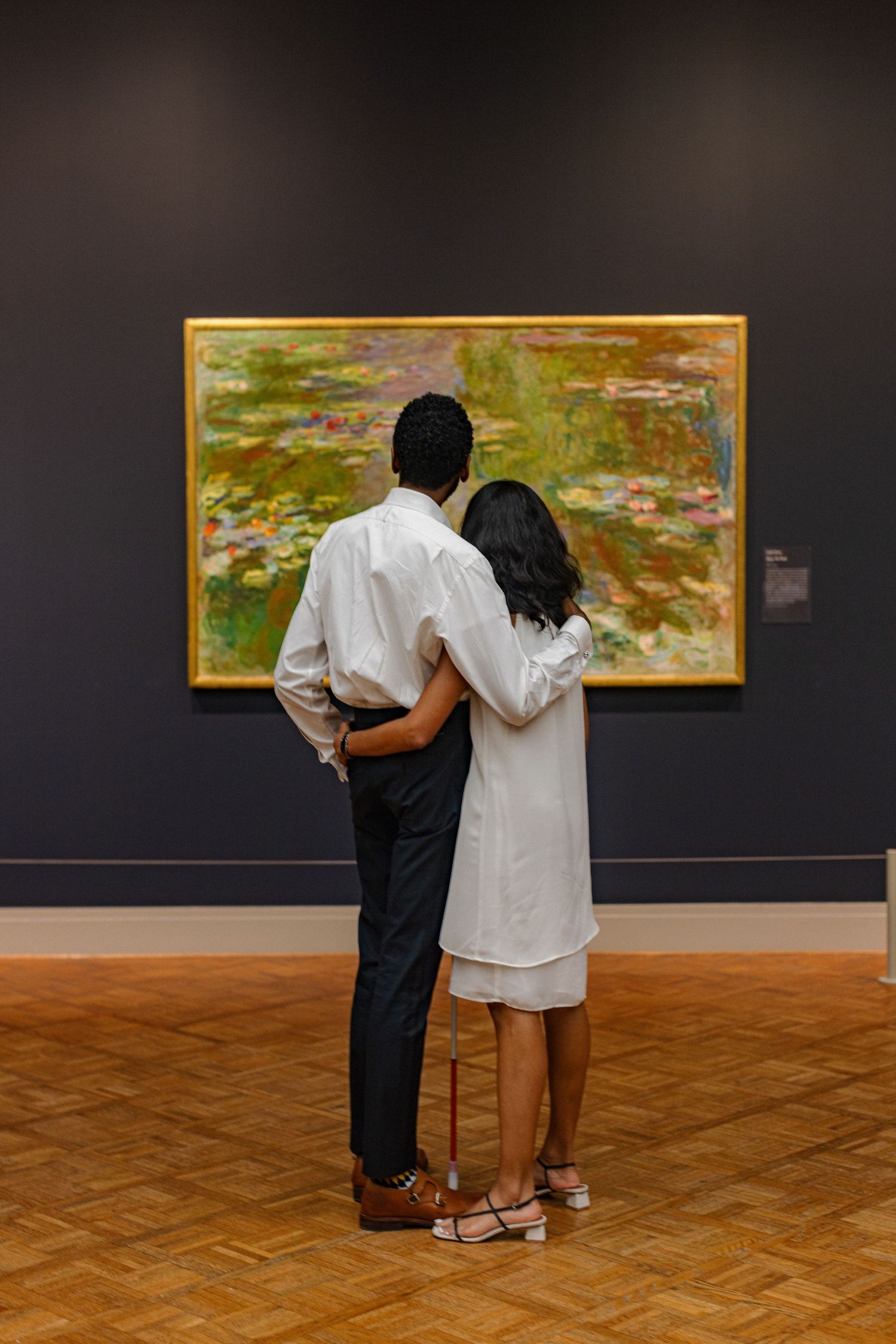 A couple viewing artwork in a museum, standing before a large impressionist painting.