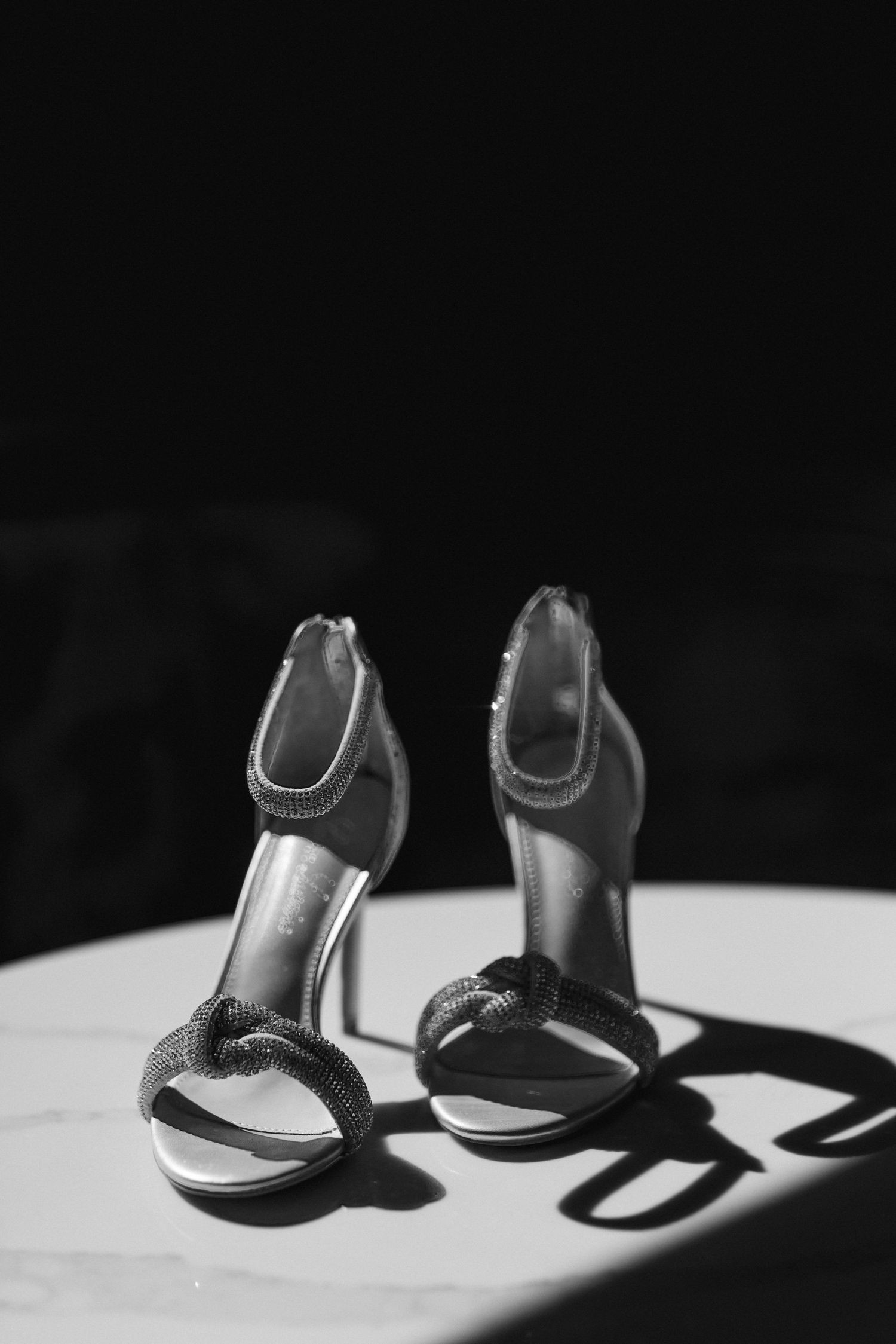 Elegant black bridal heels casting dramatic shadows on a white surface in black and white photography.