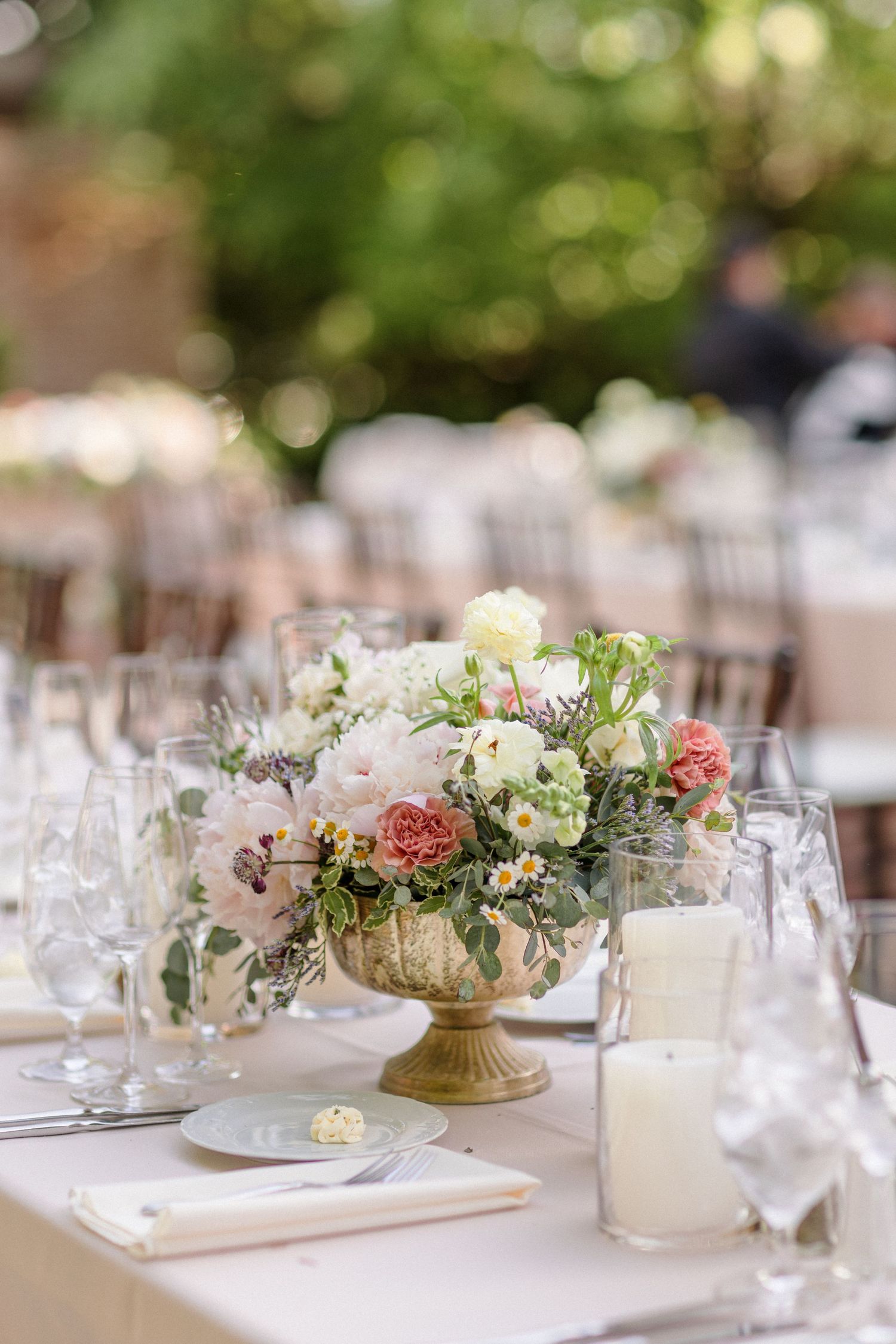 Elegant wedding table setting with pink and white floral centerpiece in a gold vintage vase.