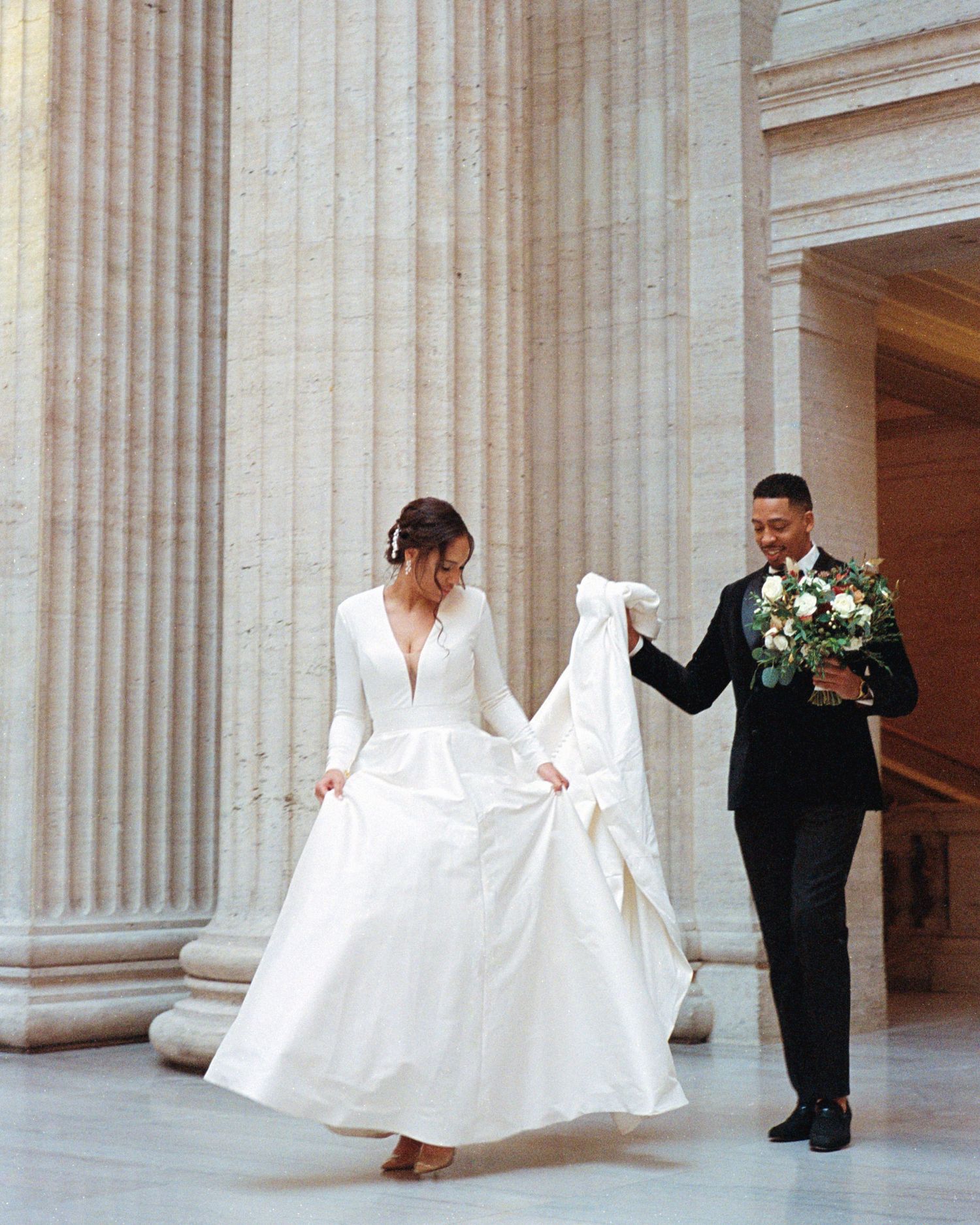 A romantic wedding moment captured between columns as the couple twirls in elegant attire.