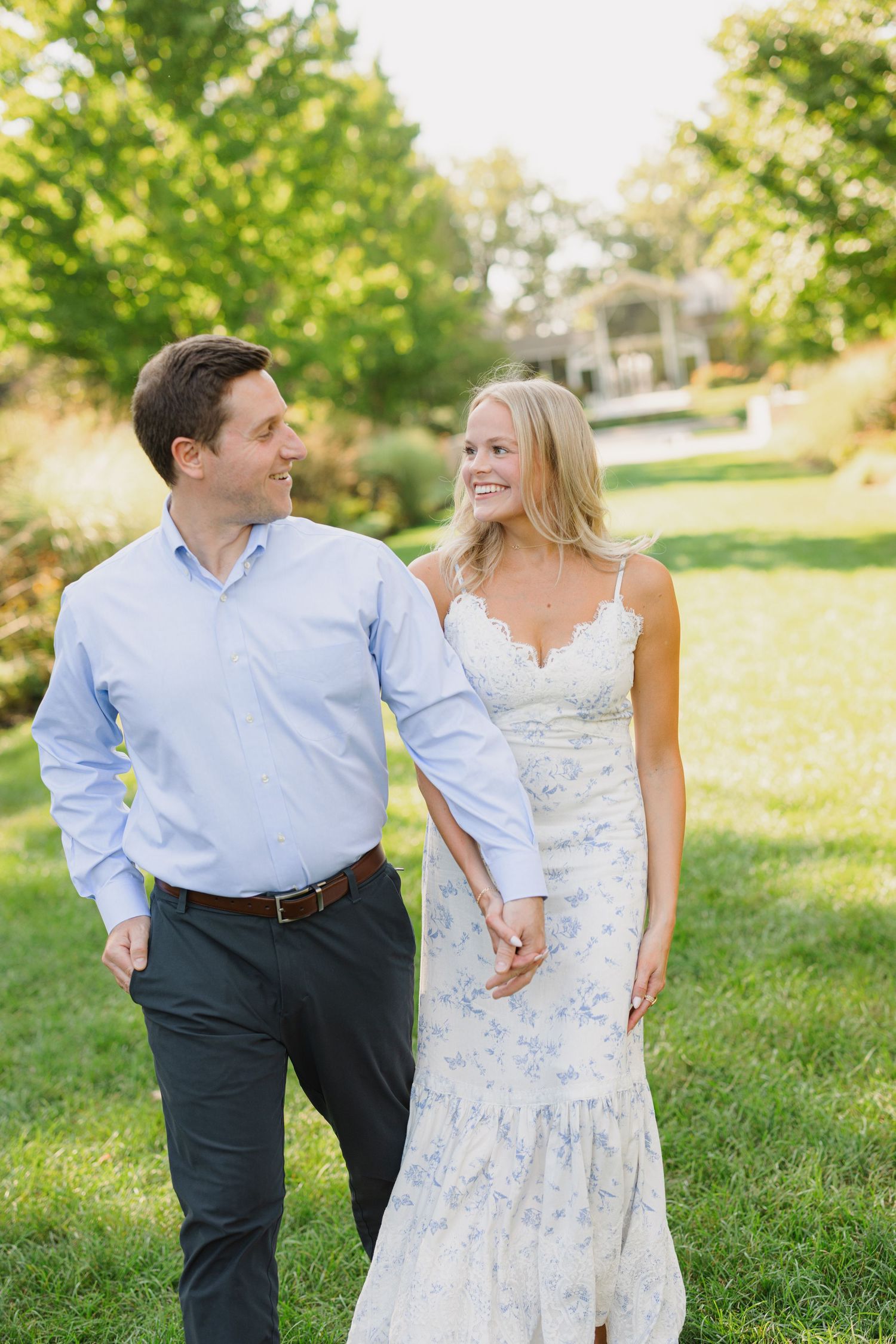 A couple in casual spring attire shares a romantic moment while walking through a sunlit grassy field.