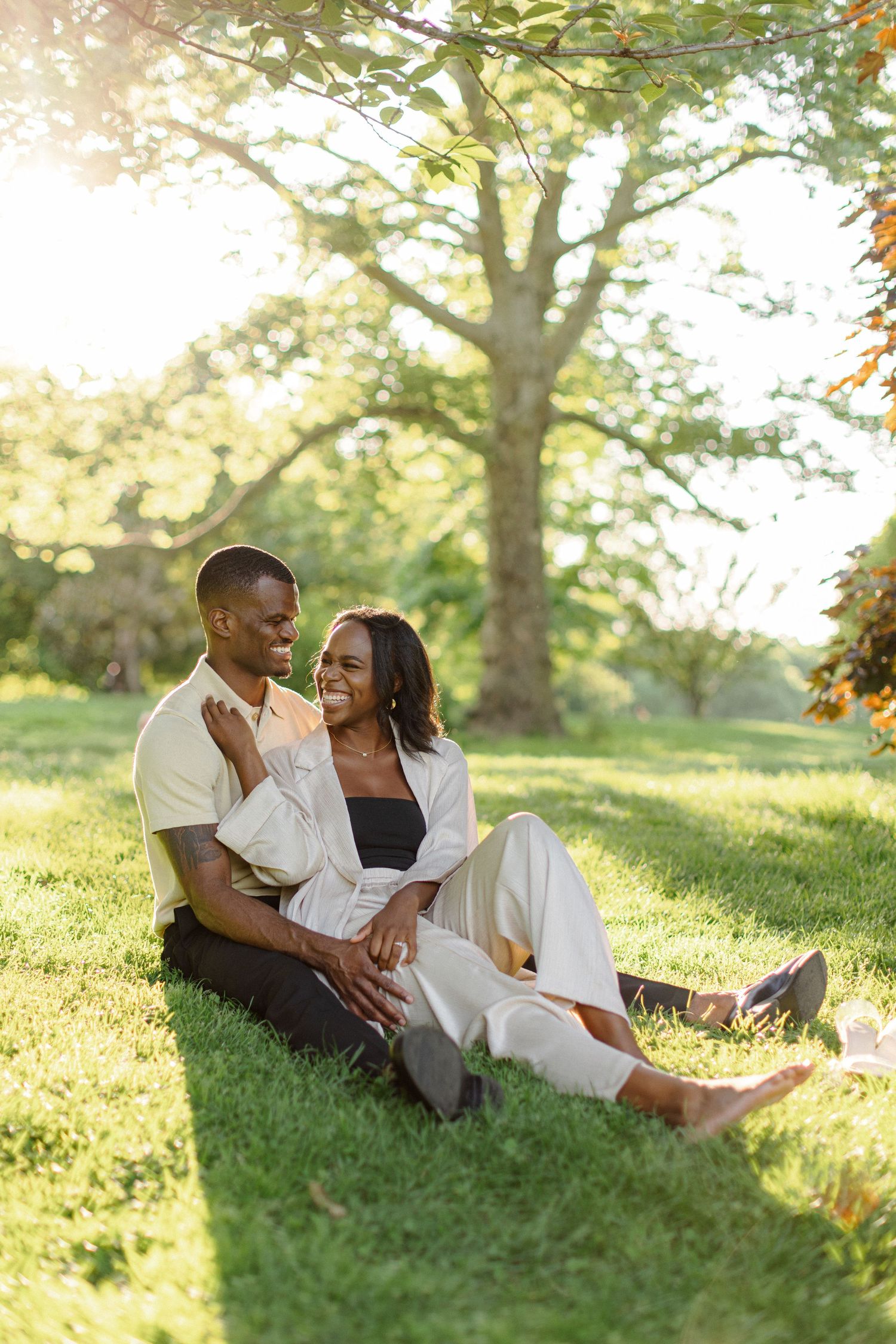 A romantic couple sitting on grass during sunset in a park setting.