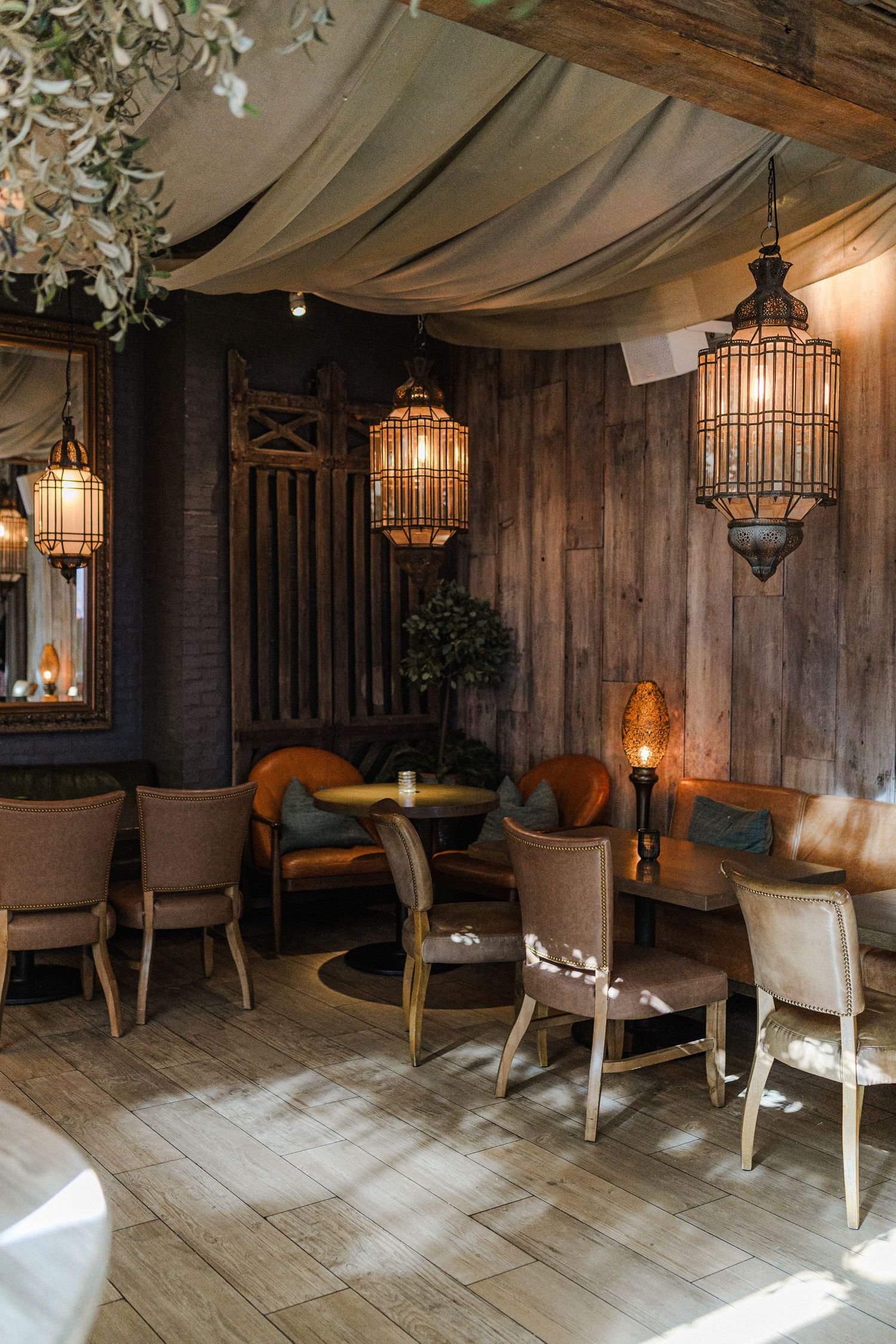 Cozy restaurant interior with hanging lanterns, draped fabric ceiling, and rustic wooden walls creating an intimate atmosphere.