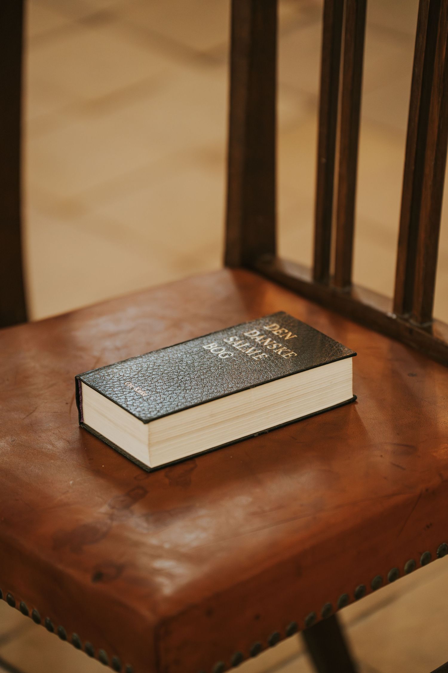 A black Bible resting on a vintage wooden chair with brown leather seat.