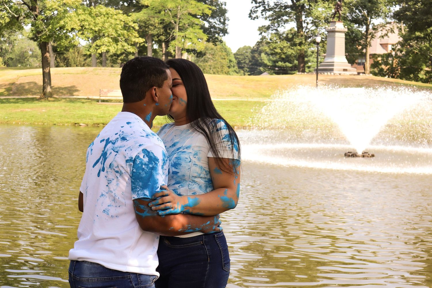 Romantic couple embracing by a fountain in a park on a sunny day.
