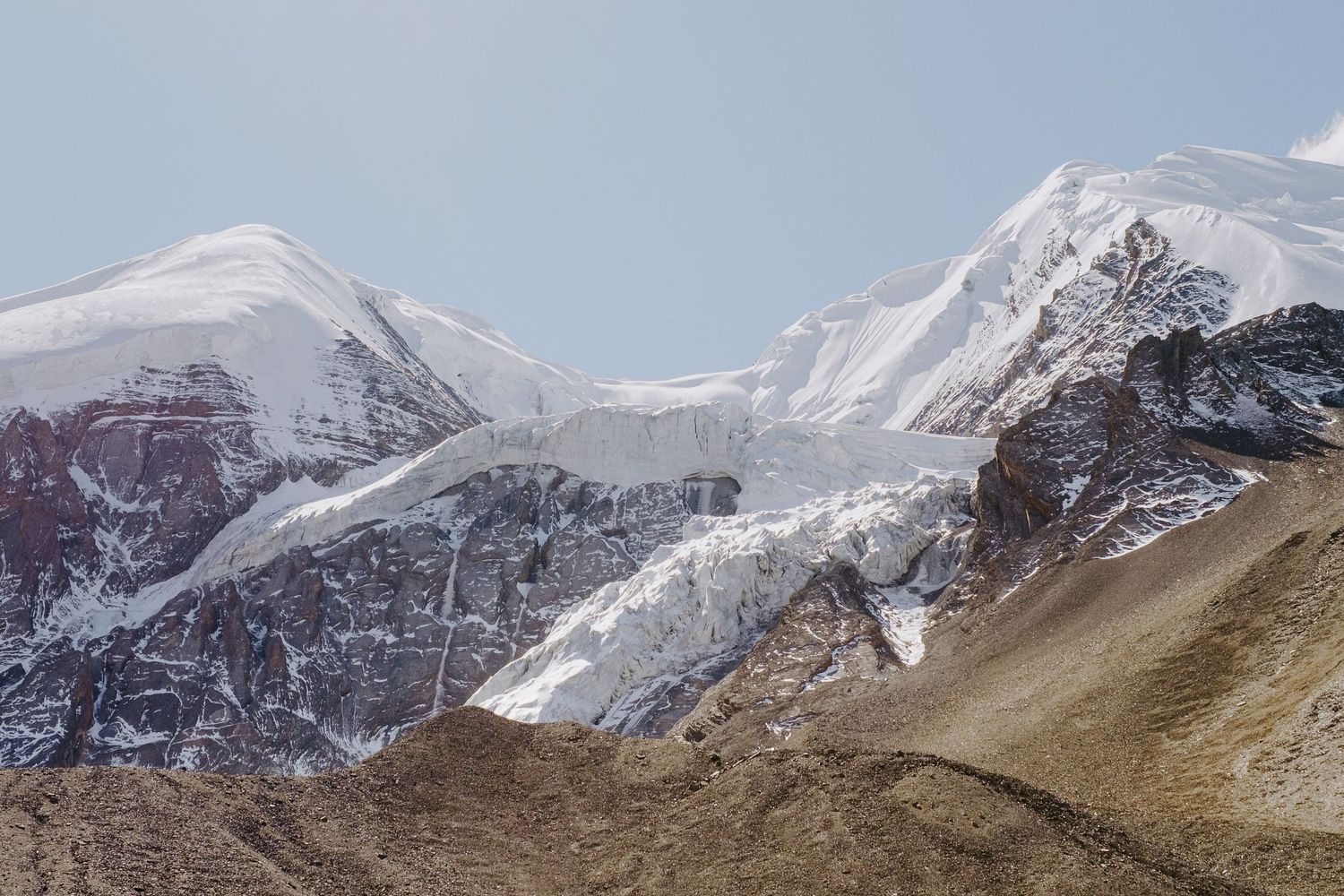 Snow-covered mountain peaks rise against a clear blue sky in the Himalayas.