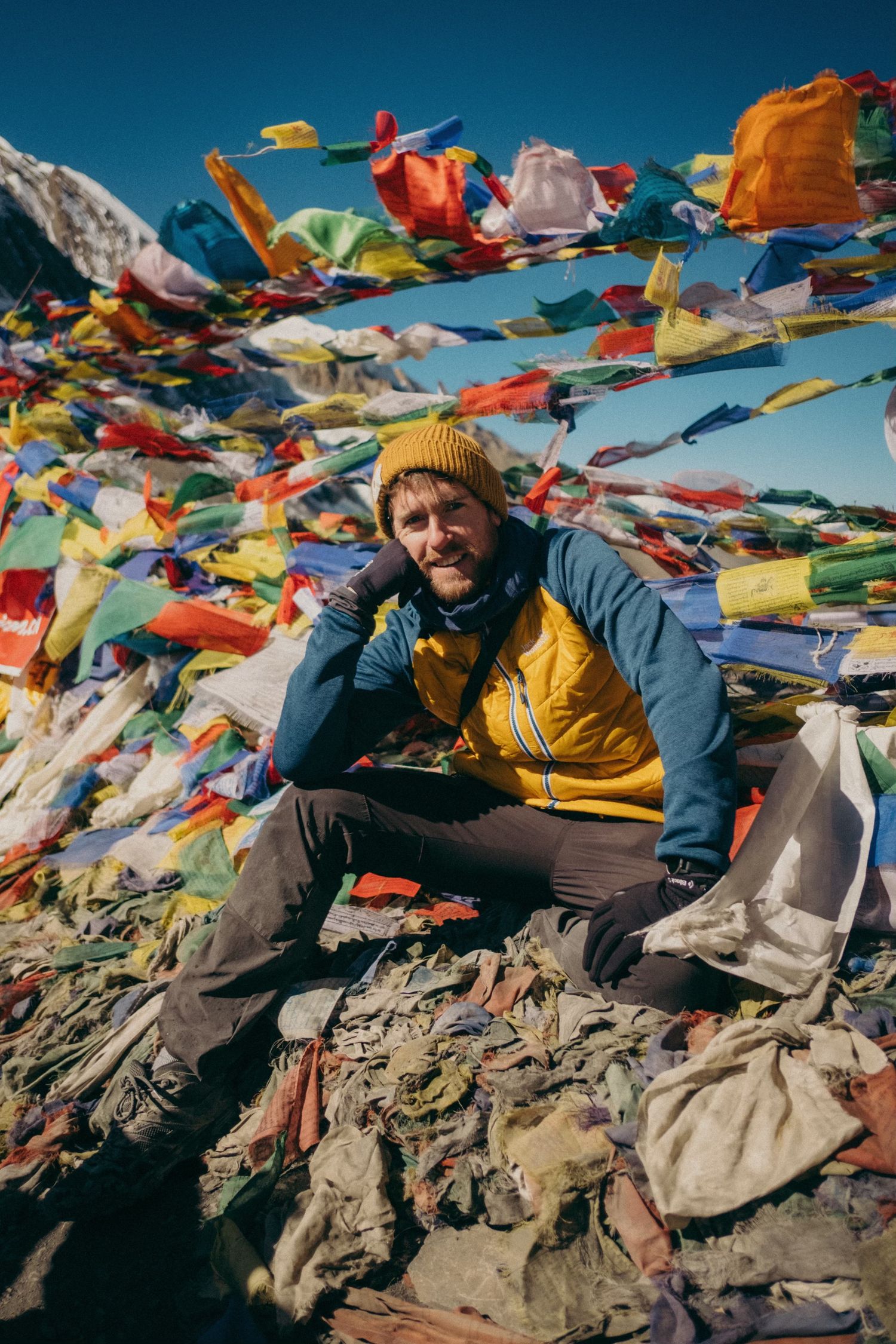 Colorful prayer flags wave against blue sky at a high mountain summit.