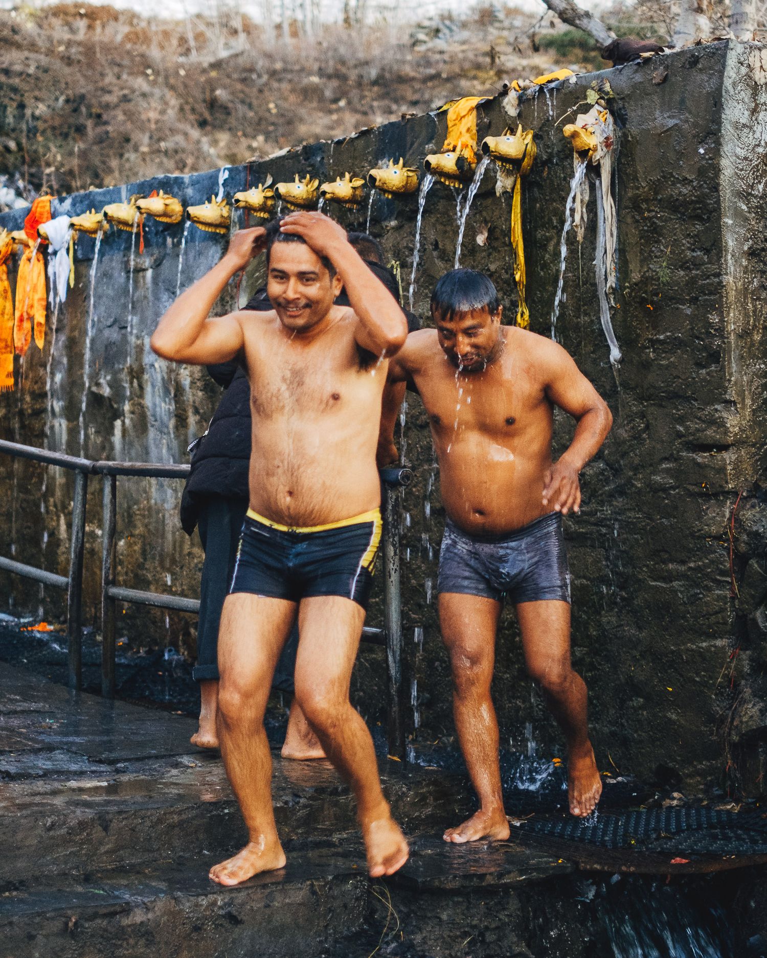 Two men refreshing themselves at an outdoor shower station.