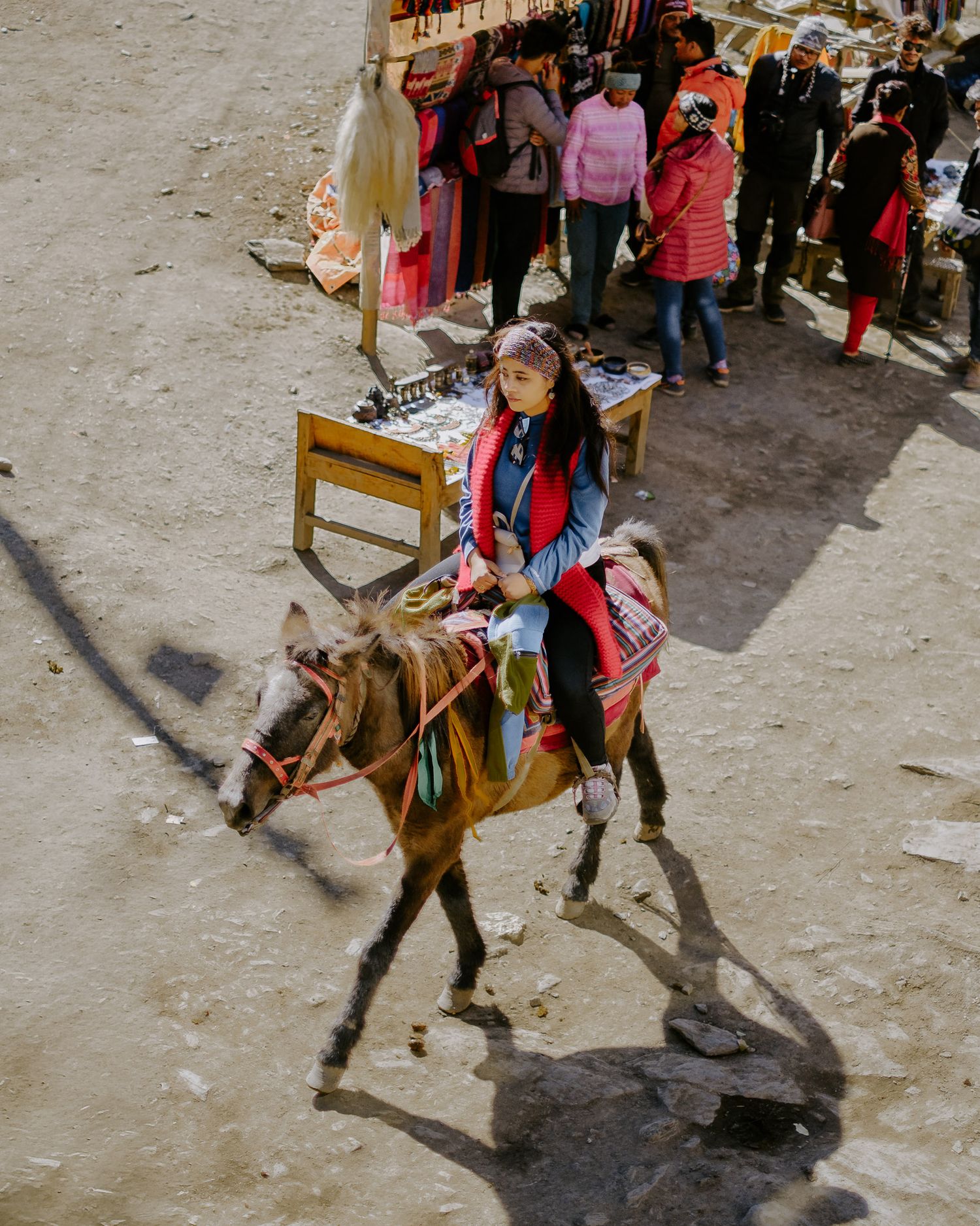 A donkey carrying supplies walks along a crowded street in what appears to be a Middle Eastern marketplace.