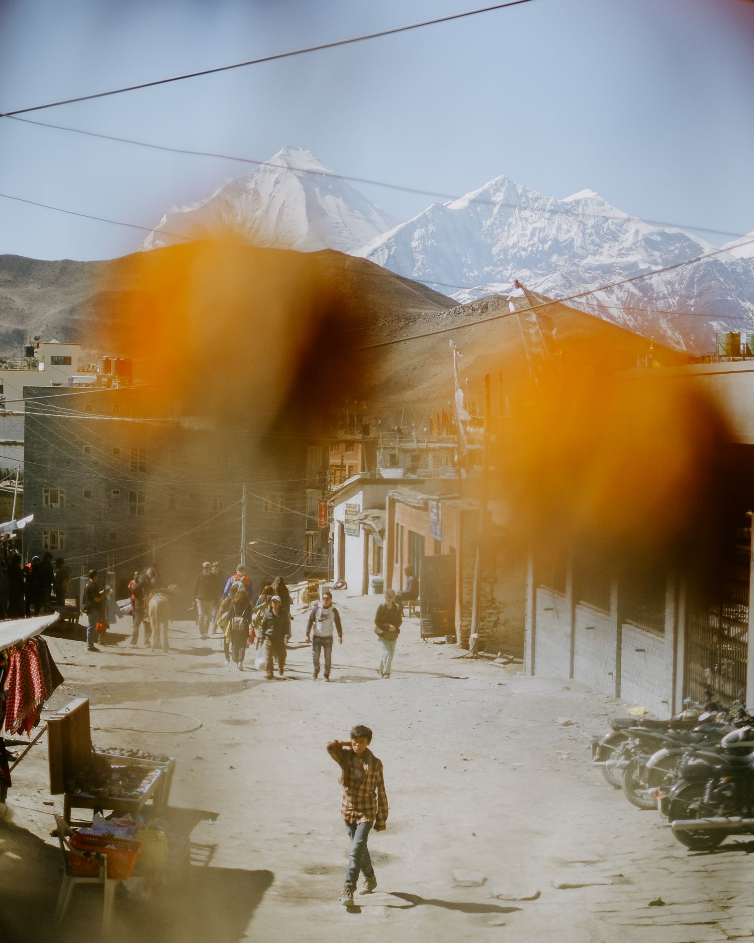 Street scene in Nepal with snow-capped Himalayan mountains in background and orange-tinted foreground blur effect.