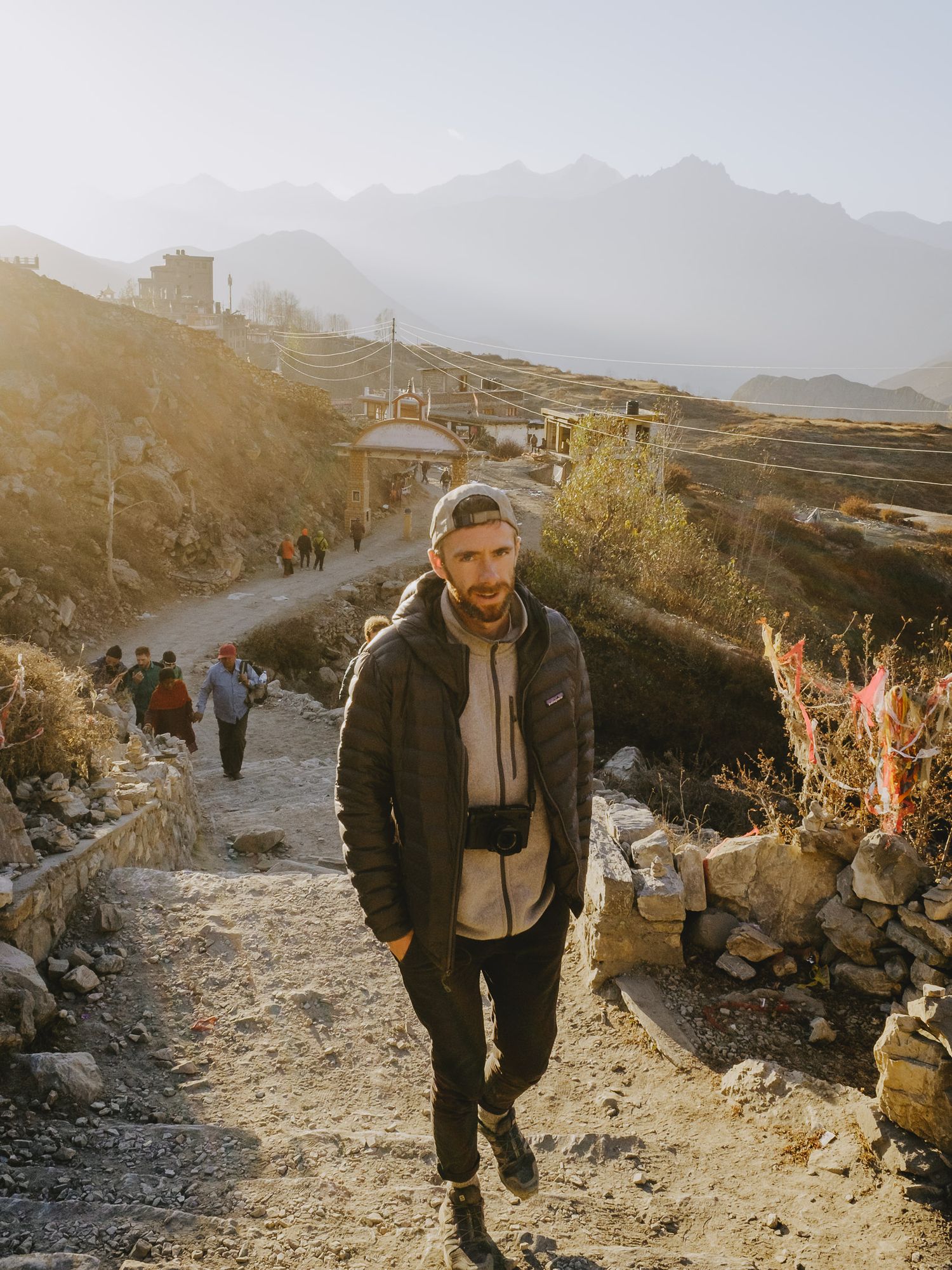 Person hiking along a rocky mountain trail at sunset with distant mountains in the background.