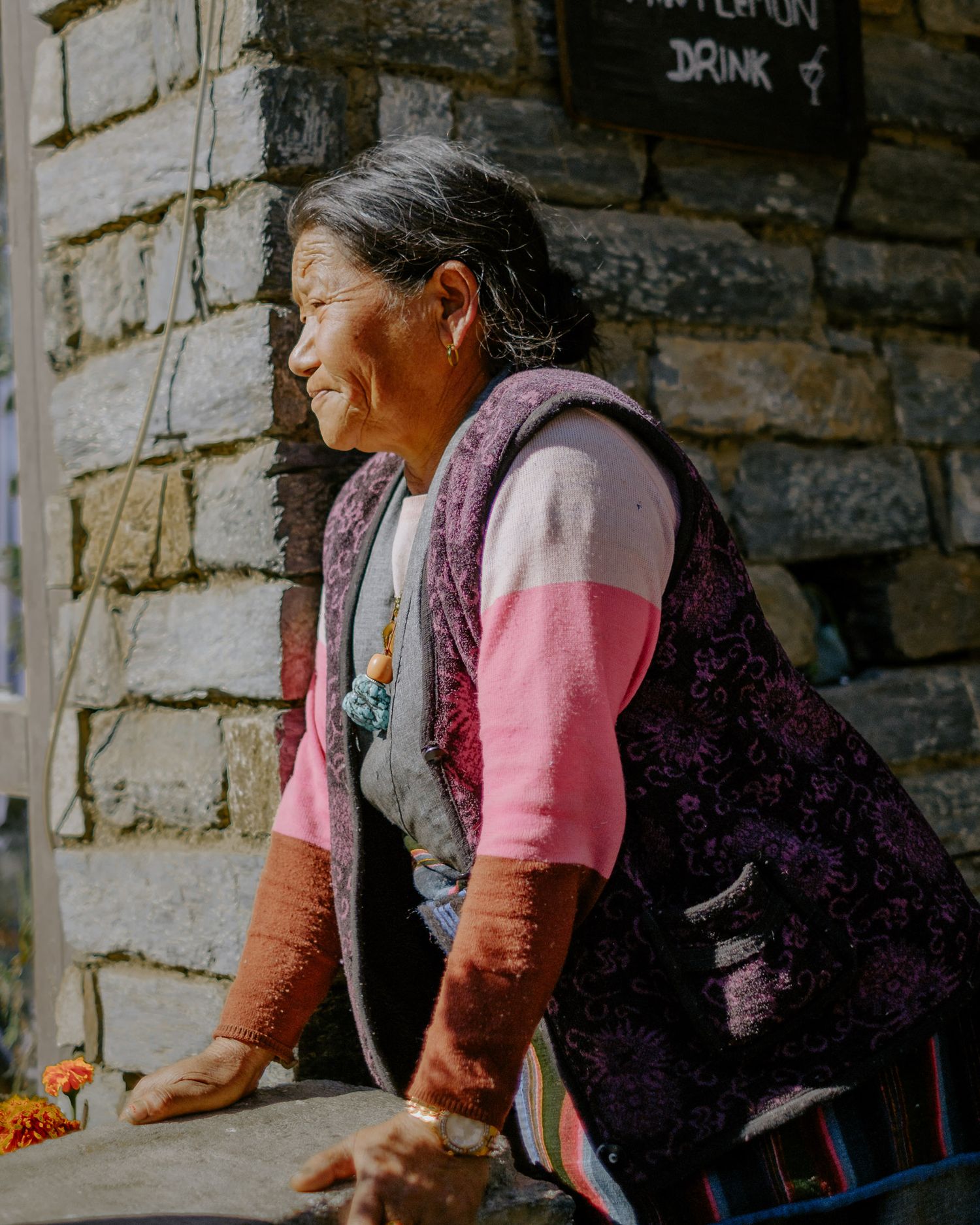Traditional Tibetan women in colorful dress sit near stone walls with prayer wheels visible.
