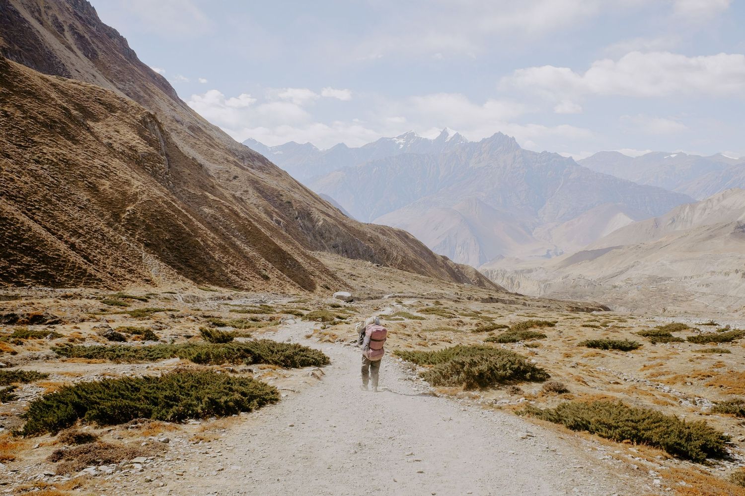 Scenic mountain valley trail stretches into distance with towering peaks on both sides.