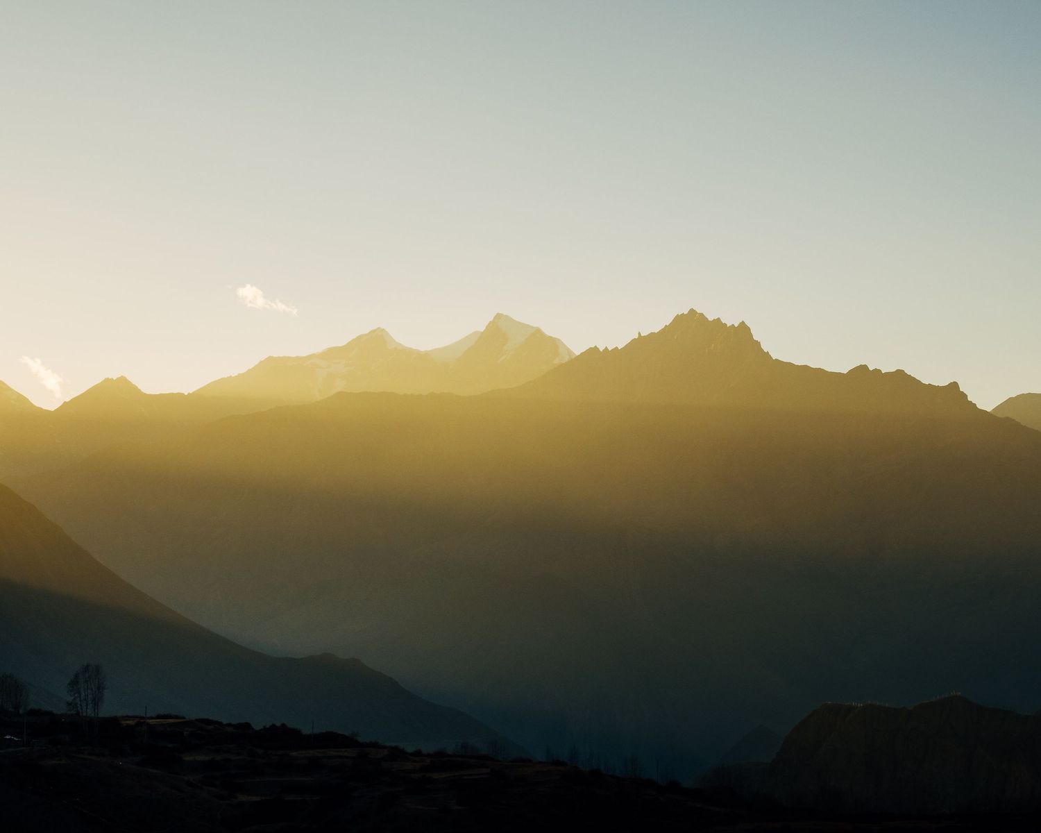 Panoramic view of silhouetted mountain peaks against a golden sunset sky creating a dramatic natural landscape.