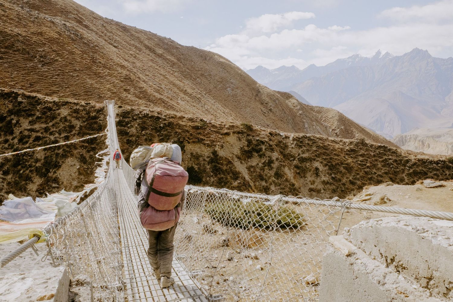 Rugged mountain landscape with winding paths and prayer flags fluttering in the wind against a cloudy sky.