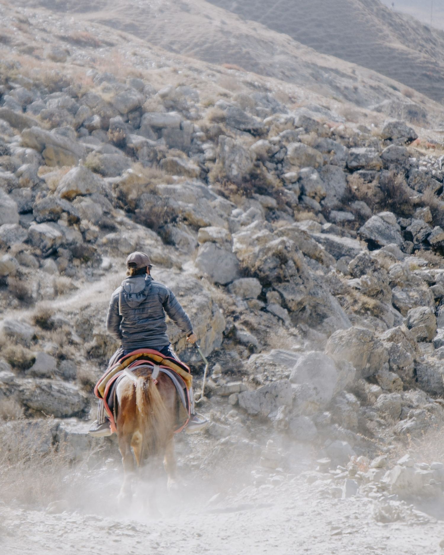 Horseback riders traversing a rocky mountain slope in a misty, rugged terrain.